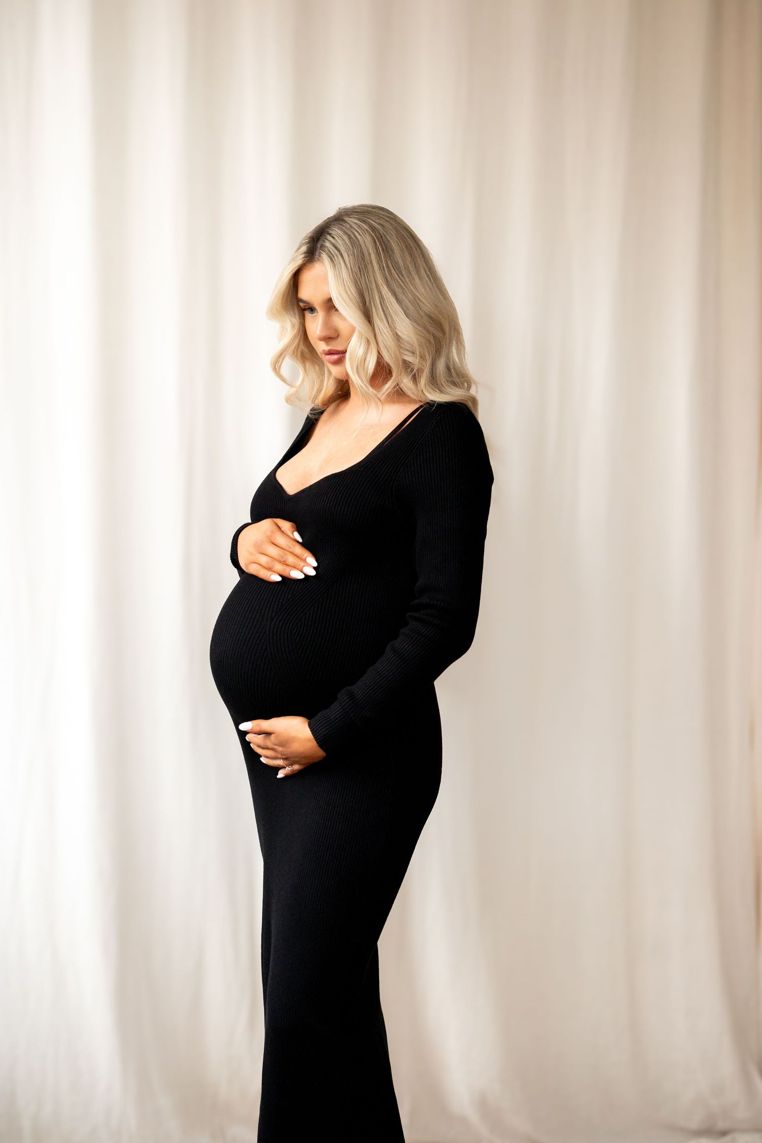 Side profile of pregnant woman in black ribbed maternity dress holding baby bump gently.