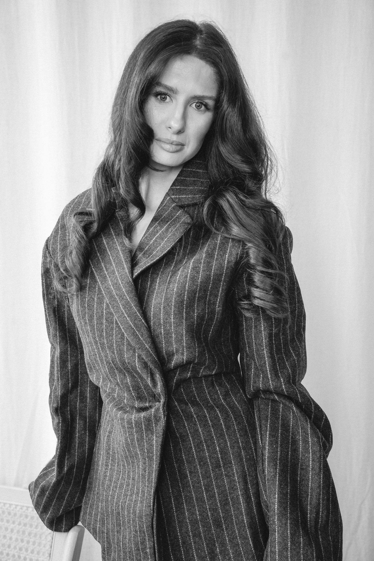 Black and white portrait of brunette woman in pinstripe oversized blazer with flowing wavy hair.