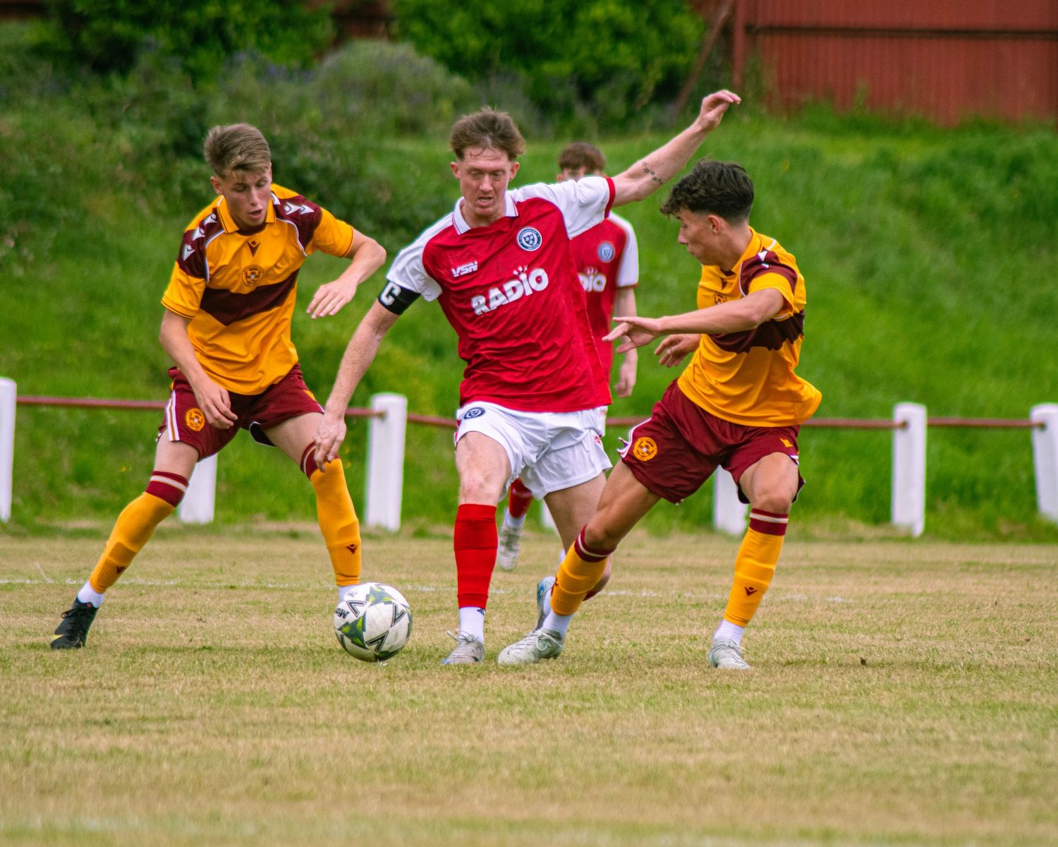 Three footballers competing for the ball during a grassroots football match.