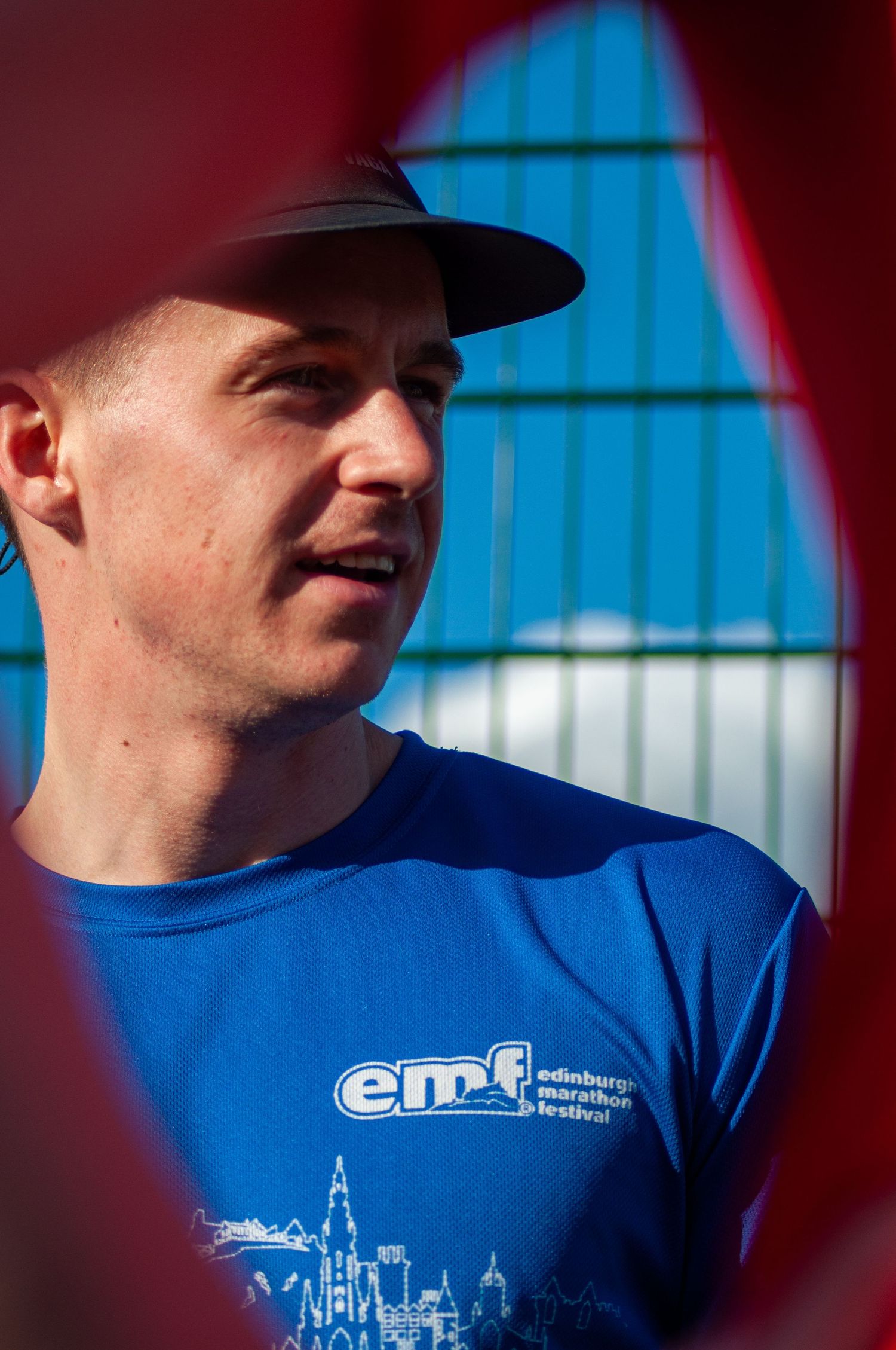 Man wearing Edinburgh Marathon Festival blue t-shirt at an outdoor athletics event.
