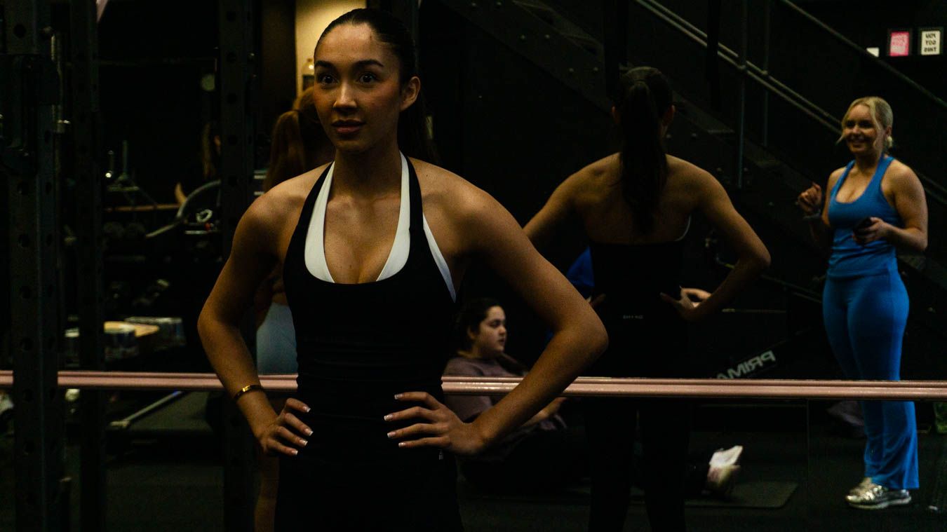 Fit woman in black sports wear posing with hands on hips in gym mirror.