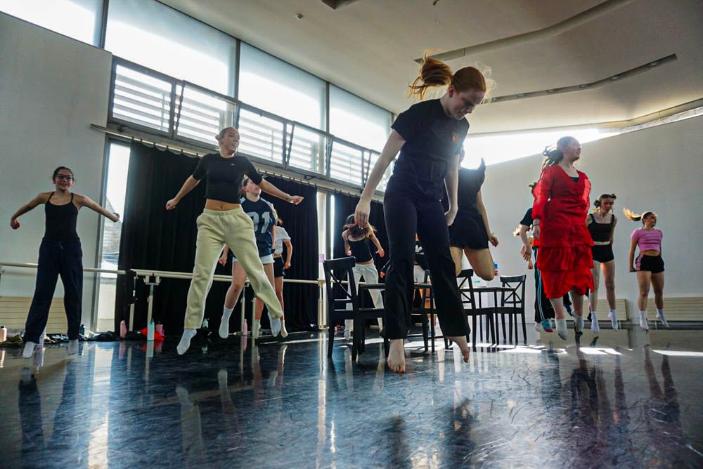 Dance students stand in a line observing instructor seated on floor during contemporary dance class.