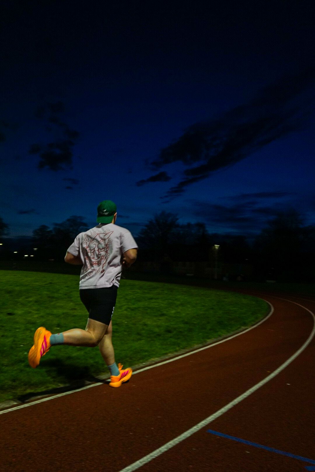 Male runner seen from behind on a curved athletics track under a dramatic twilight sky.