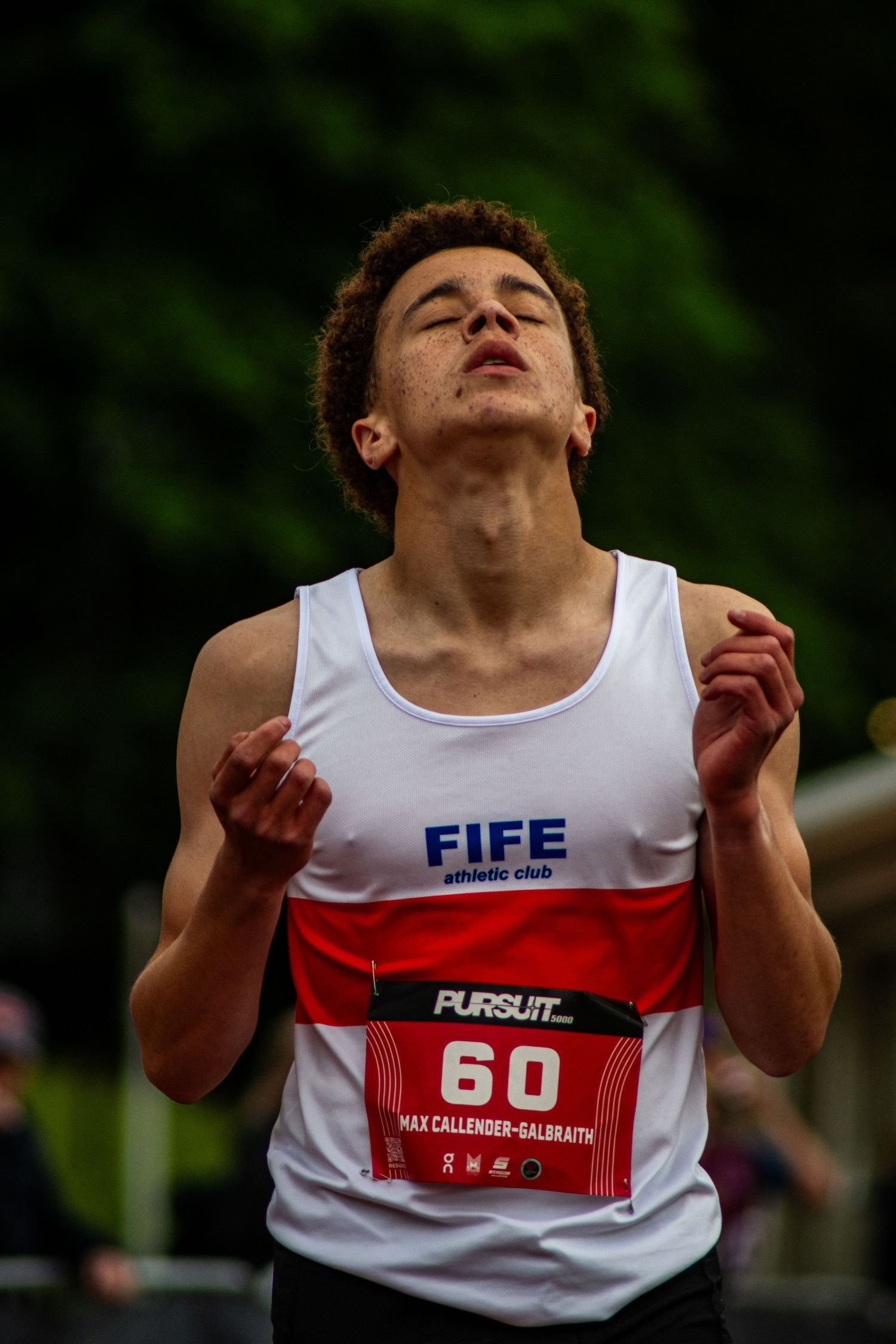Runner Max Callender-Galbraith wearing bib 60 for Fife Athletic Club competes in a track race with eyes closed.