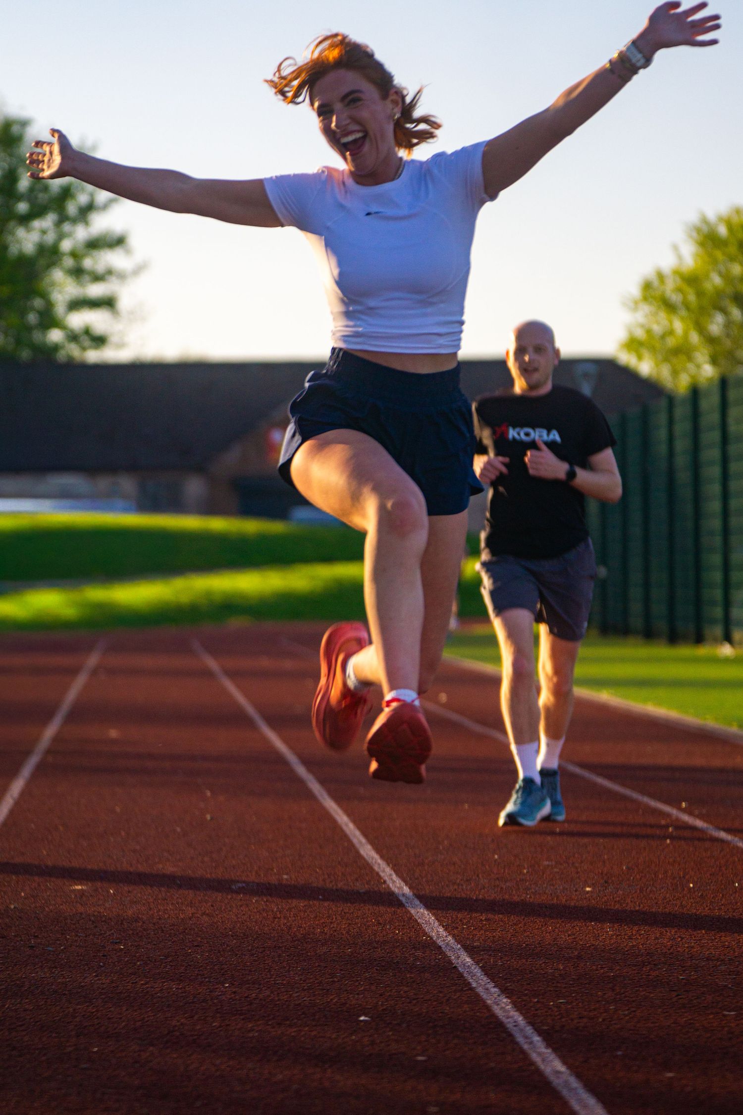 Excited female athlete celebrates finishing a track run with arms raised in triumph.