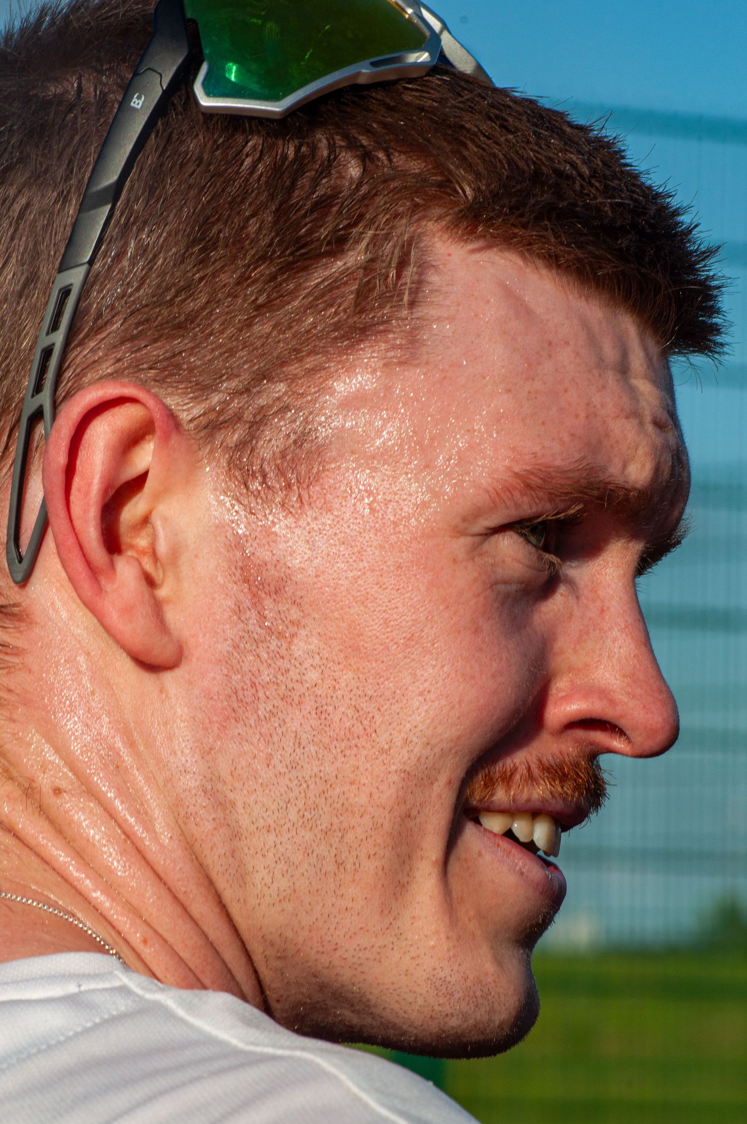 Close-up portrait of a sweaty male athlete smiling with green sunglasses on his head.
