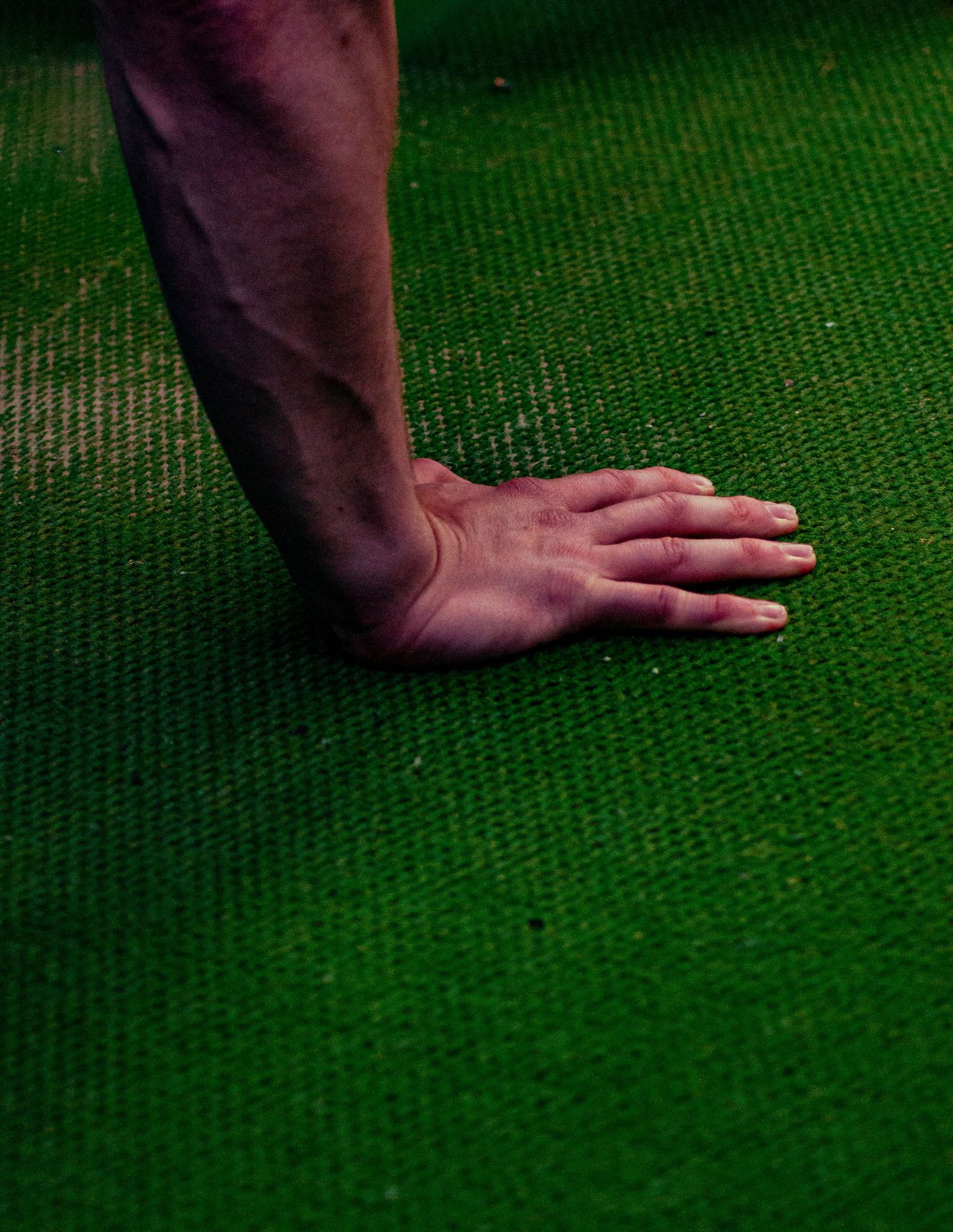 Close-up of a hand pressed flat on a bright green artificial turf surface.
