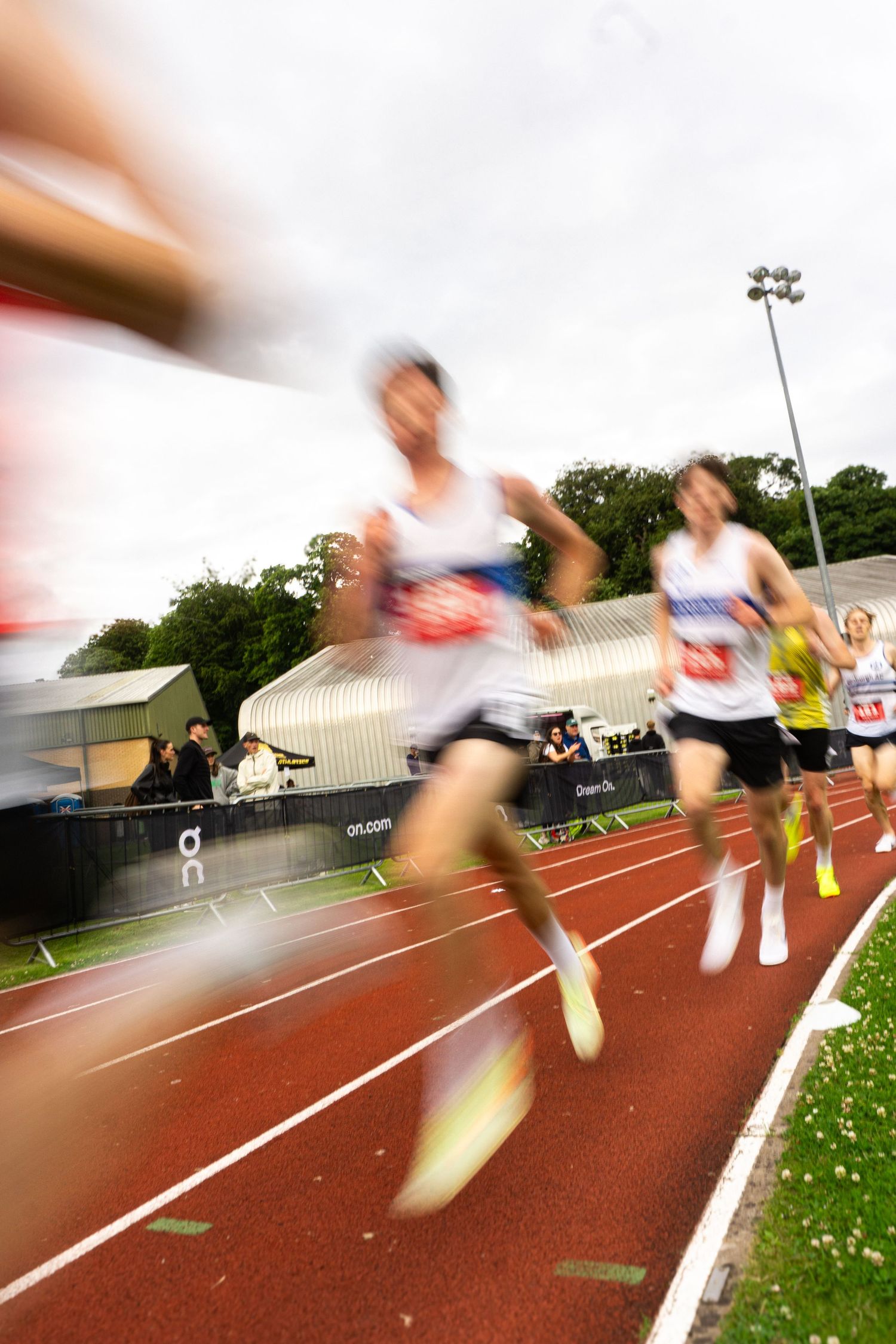 Blurred motion photo of runners racing on a red athletic track during a competitive outdoor track and field event.
