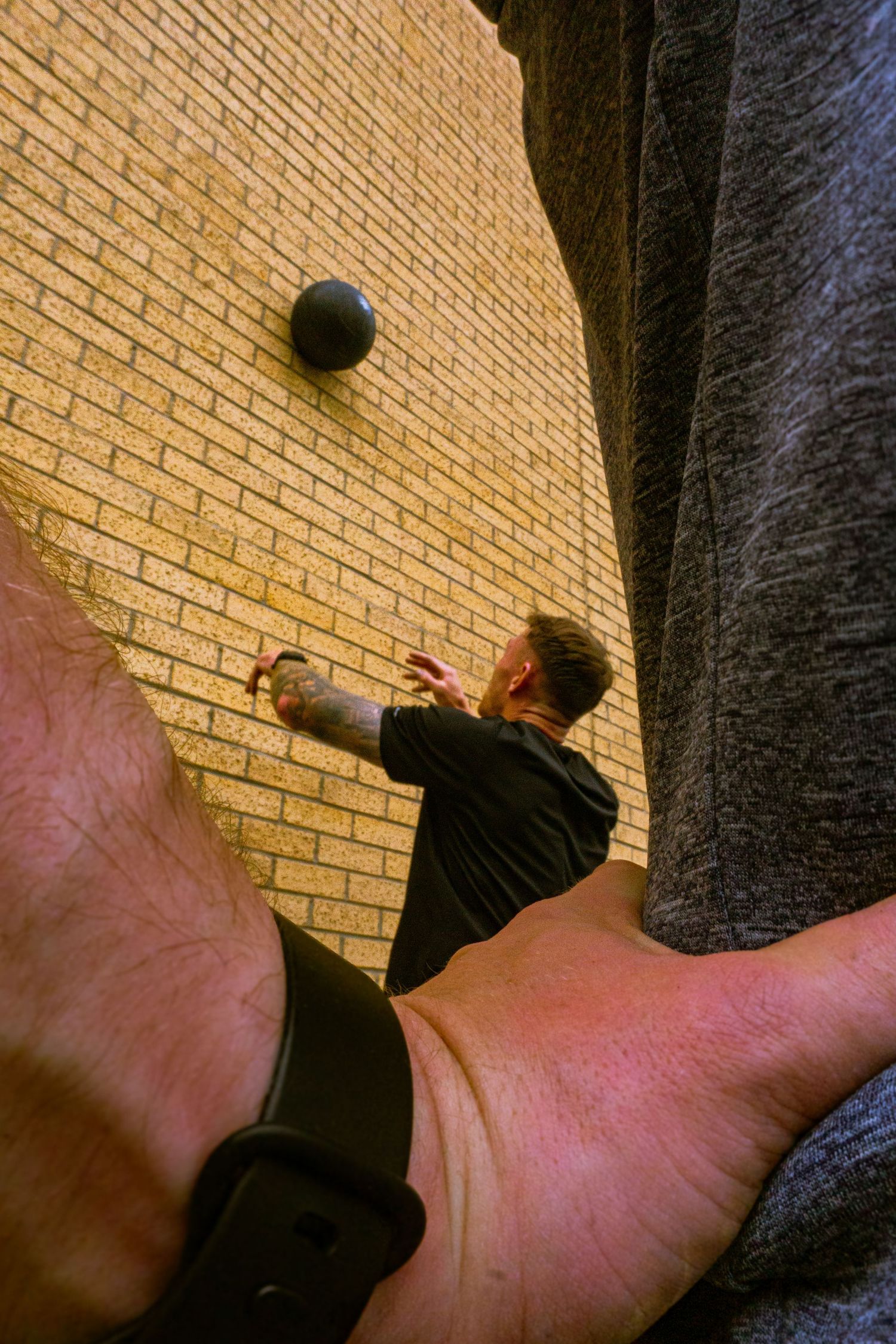 Man in black shirt throwing a ball against a brick wall, captured from an overhead perspective.