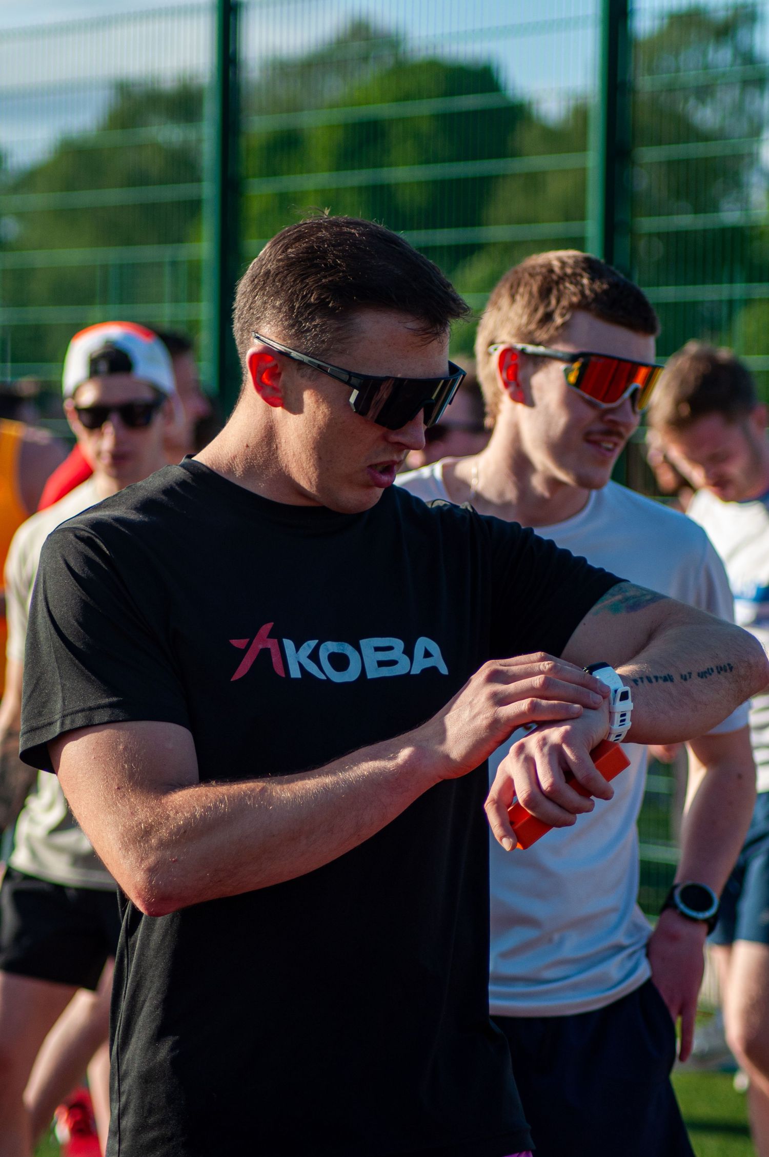 Muscular man in KOBA black t-shirt checking his sports watch at an athletics event.