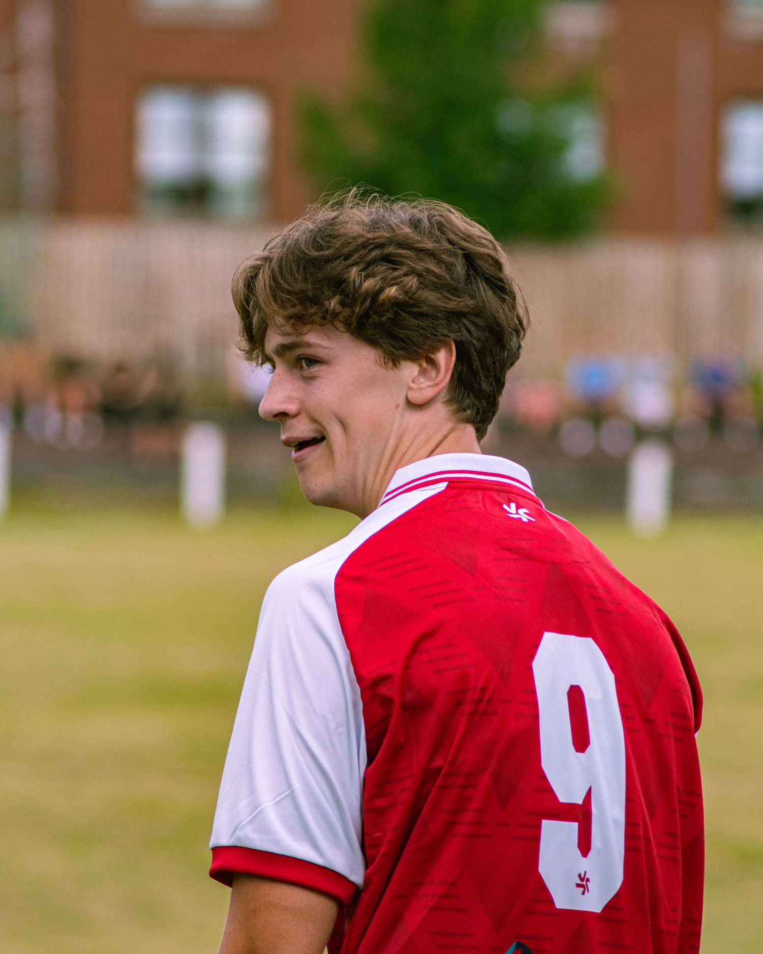 Young male soccer player wearing red and white number 9 jersey looks sideways on the football pitch.