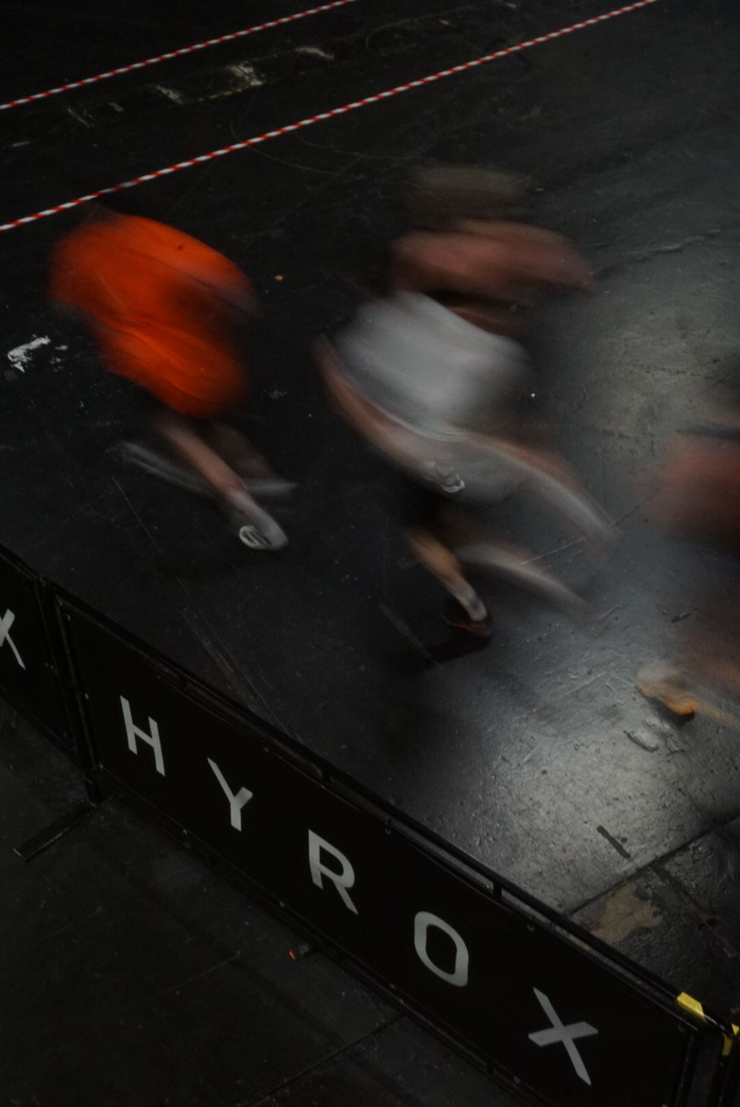 Motion-blurred overhead view of runners passing a HYROX branded barrier during competition.