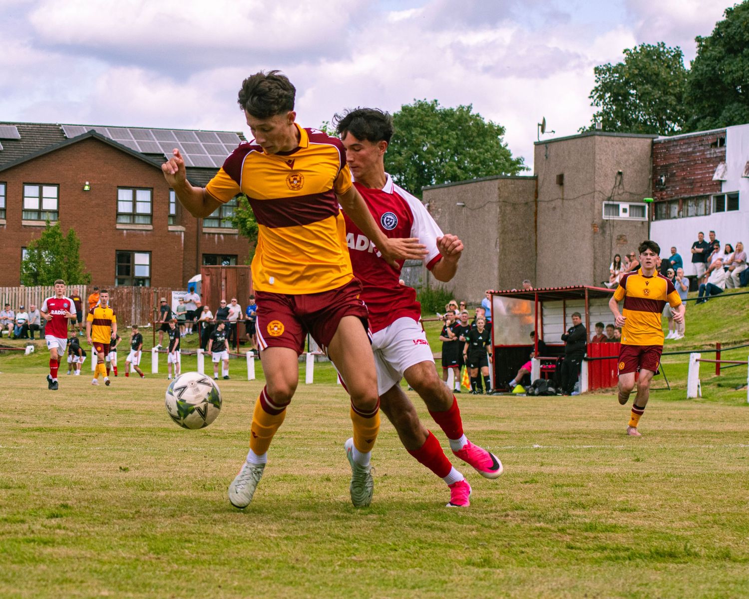 Two youth soccer players battle for the ball during a competitive match on a grass field, wearing red and yellow kits.