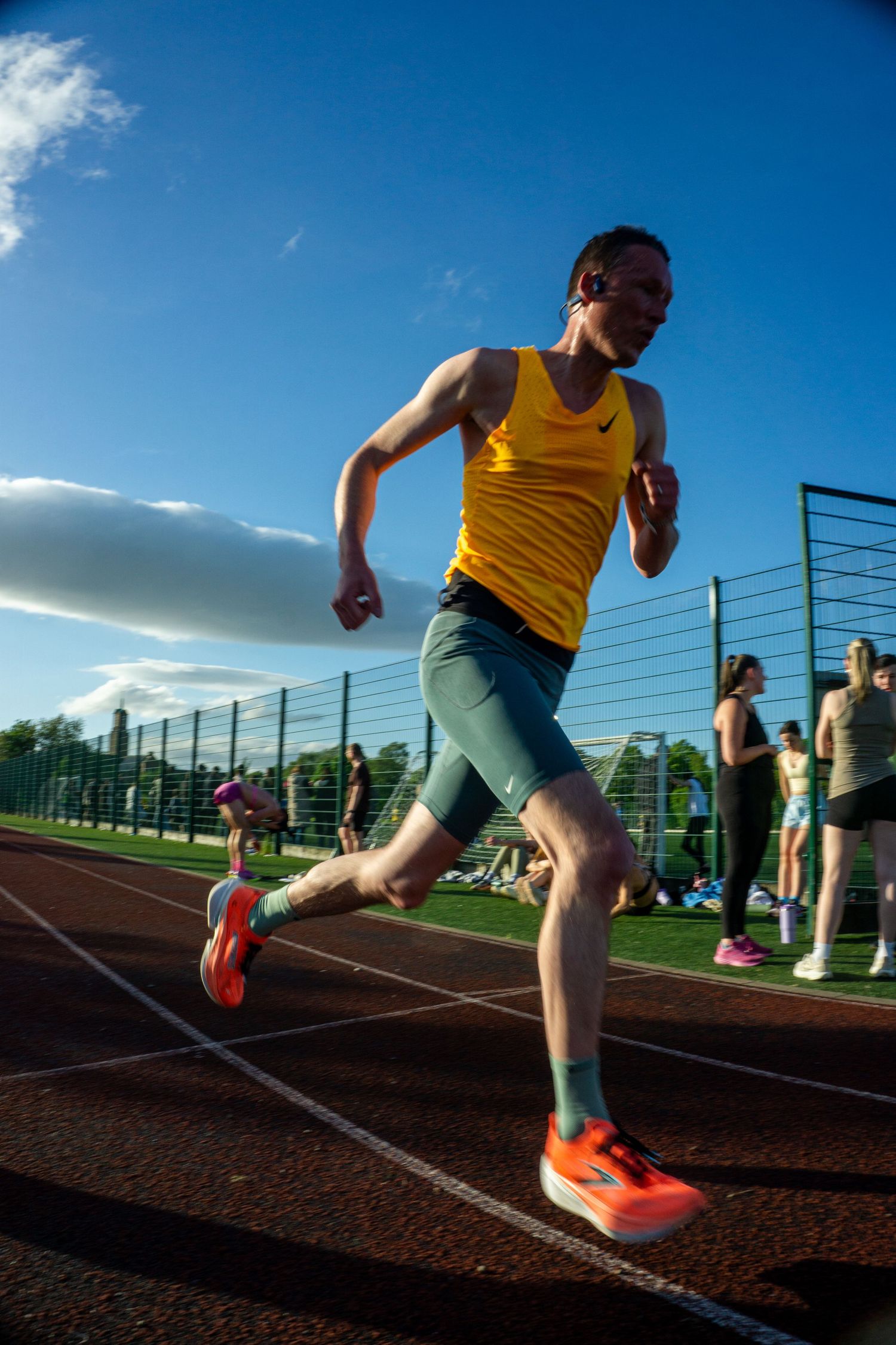 Male runner in yellow Nike vest and teal shorts sprinting on a red athletics track.