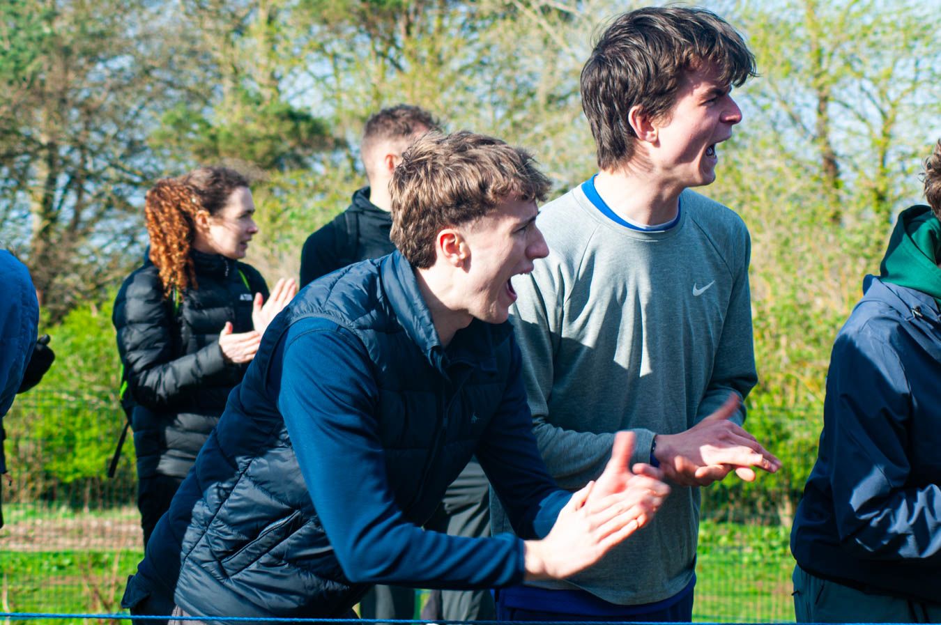 Young man clapping and cheering enthusiastically at outdoor sporting event.