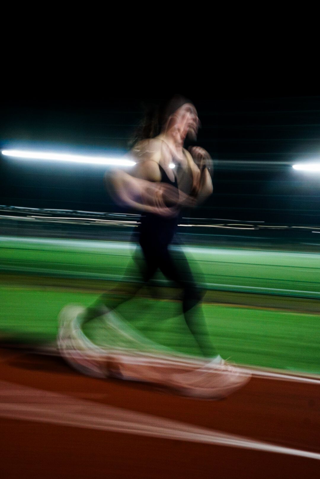 Dynamic motion blur photo of a female athlete sprinting on a red running track at night.