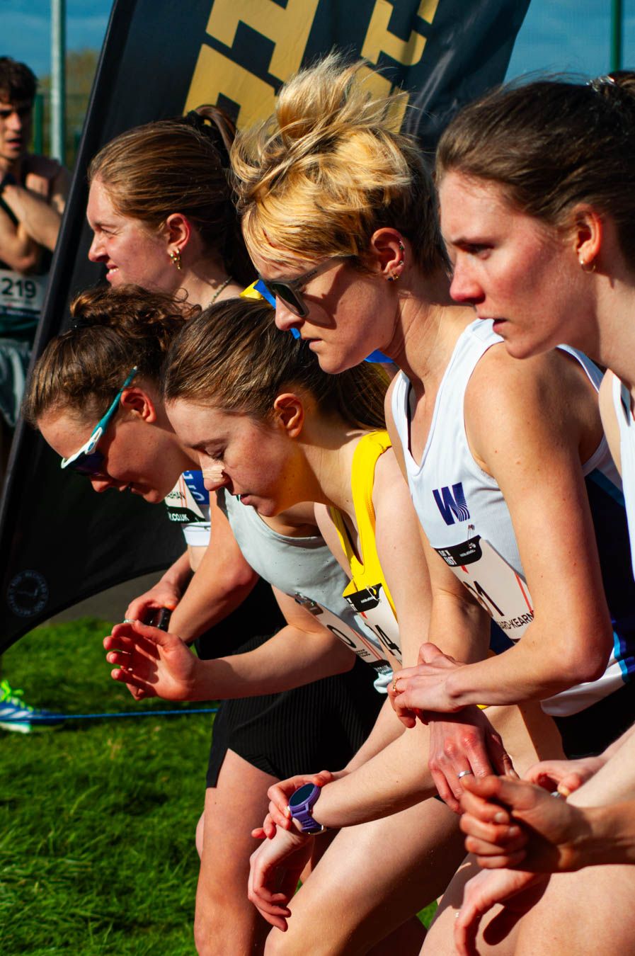 Female athletes focused at starting line of competitive running race outdoors.