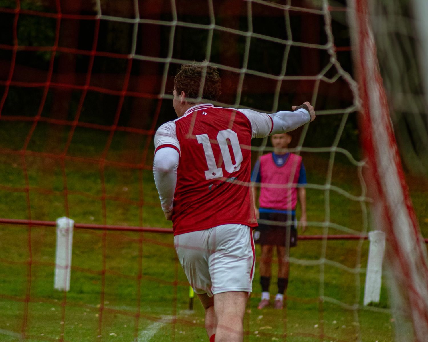Soccer player wearing number 10 red and white jersey celebrates a goal near the net on a green field.