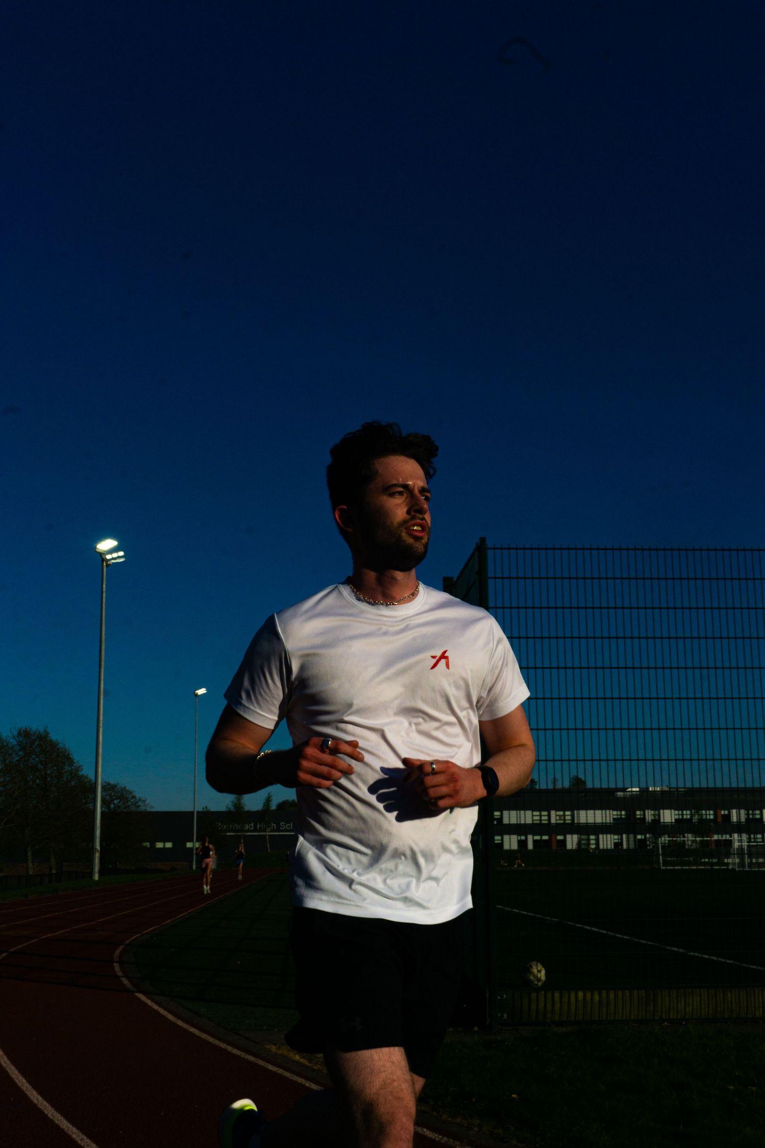 Male runner in white t-shirt on red track under deep blue evening sky.