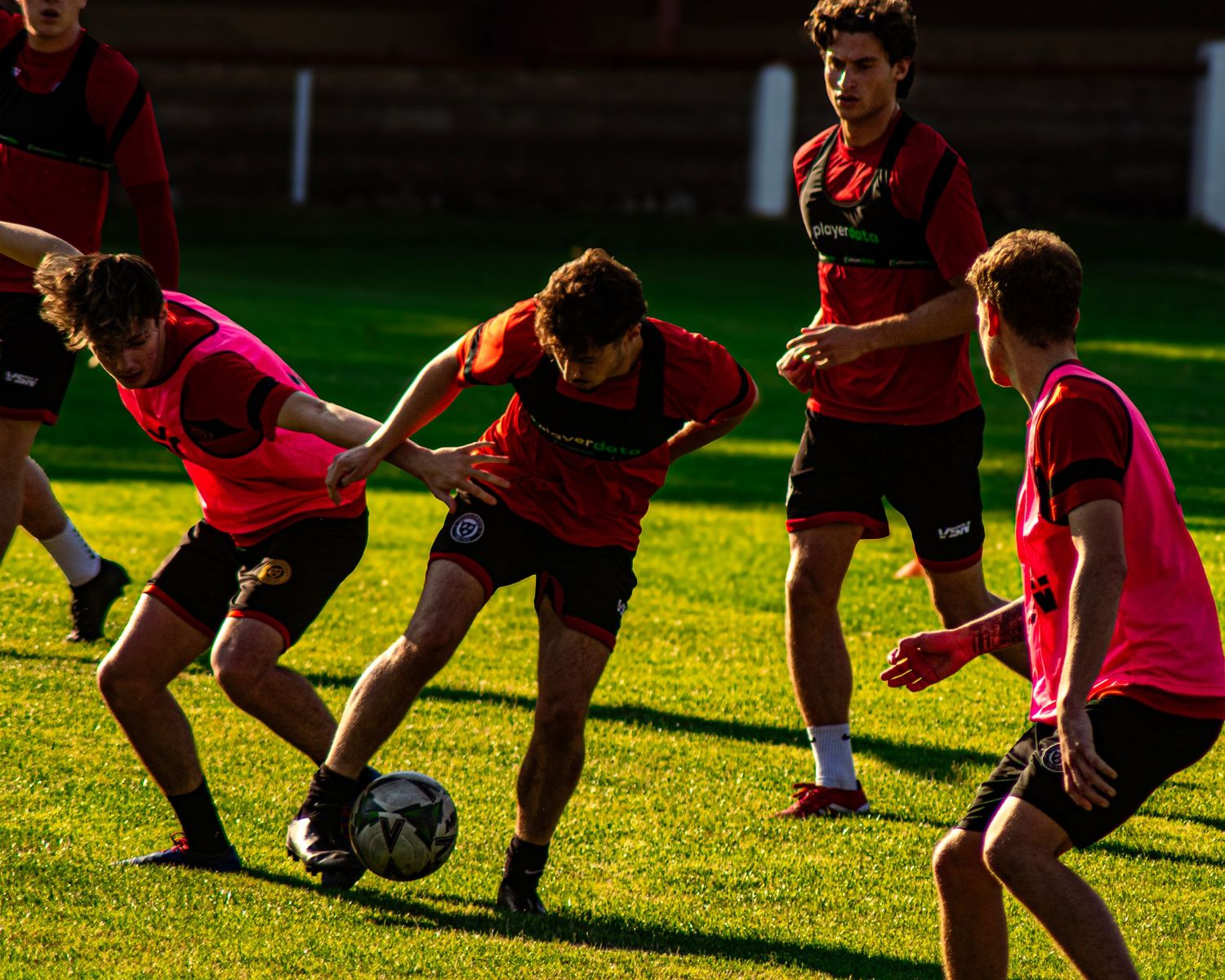 Soccer players in red uniforms compete for the ball during an outdoor training session on a green grass field.
