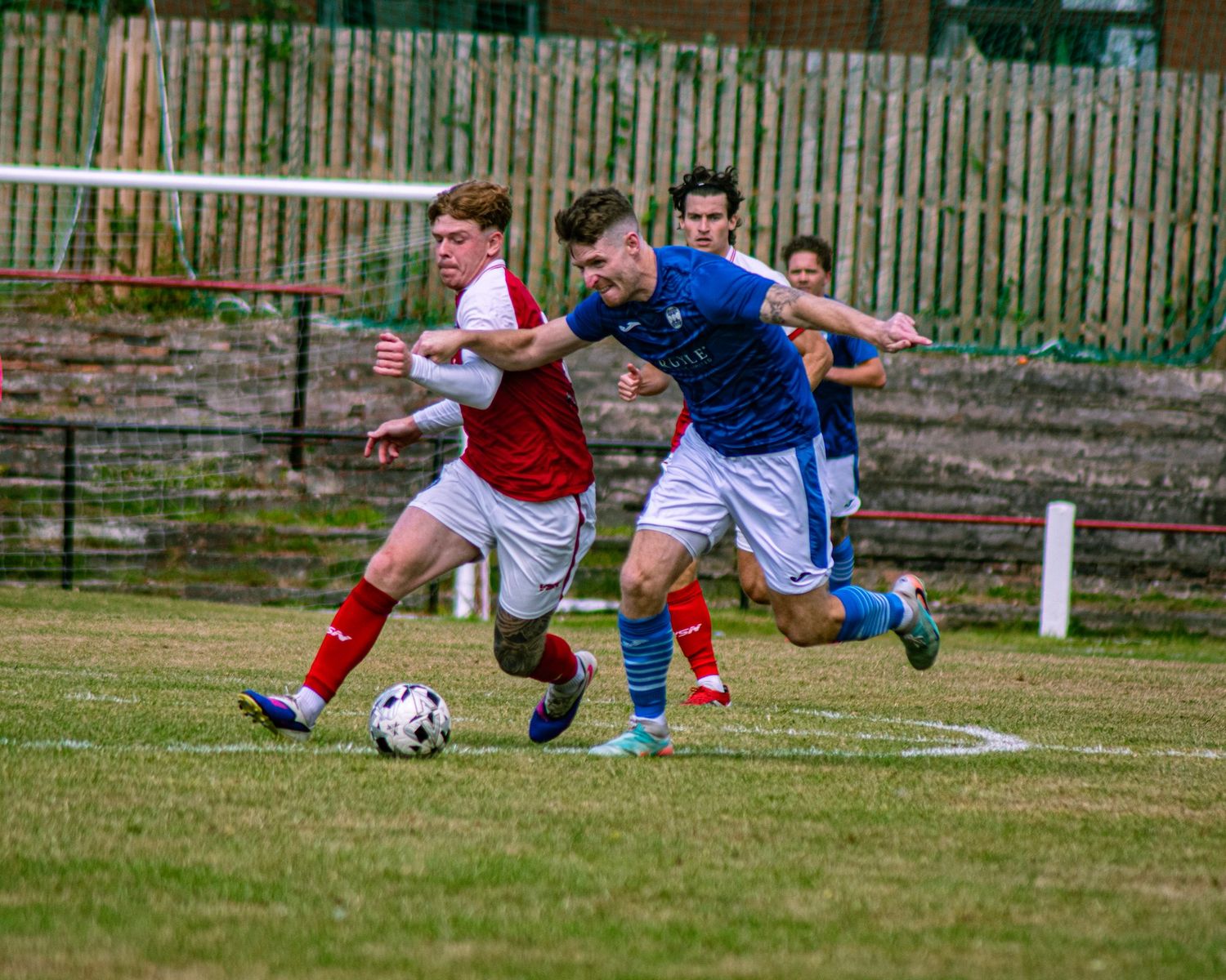 Two youth soccer players compete for the ball during a match, one in red and white, the other in blue.