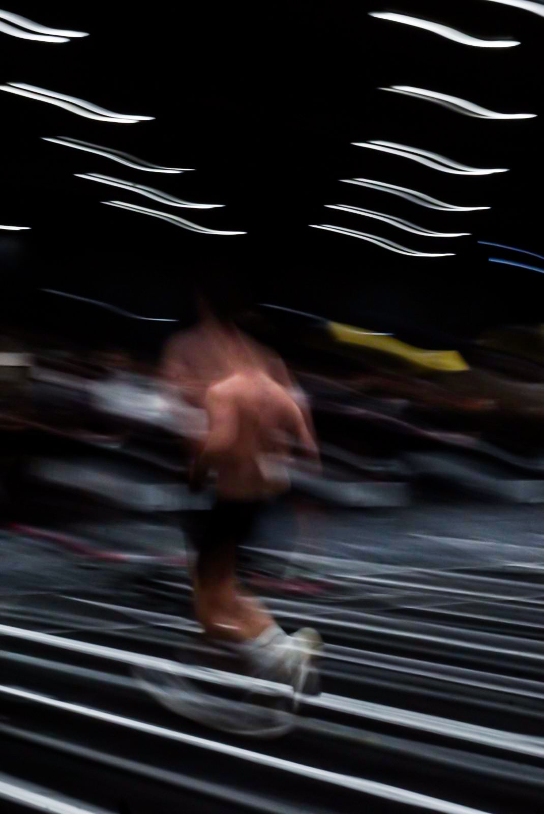 Dynamic motion blur image of shirtless athlete sprinting across a gym floor during competition.