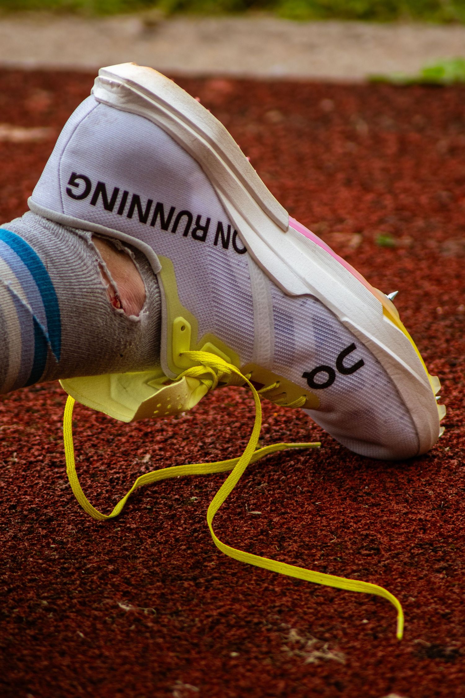 Worn white On Running track spike shoe with yellow laces on a red running track surface.