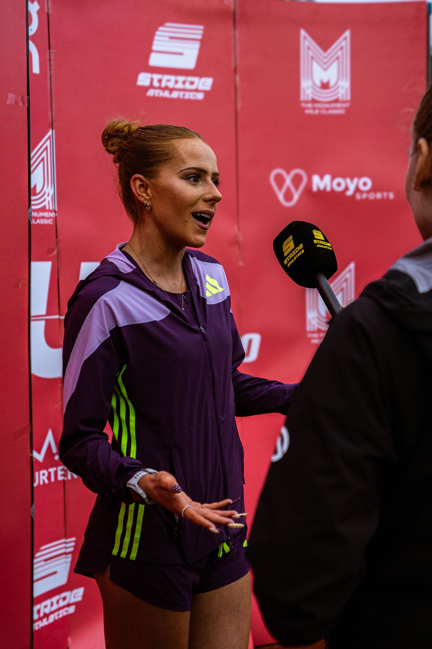 Female athlete in purple Adidas tracksuit being interviewed at Moyo Sports event with microphone.