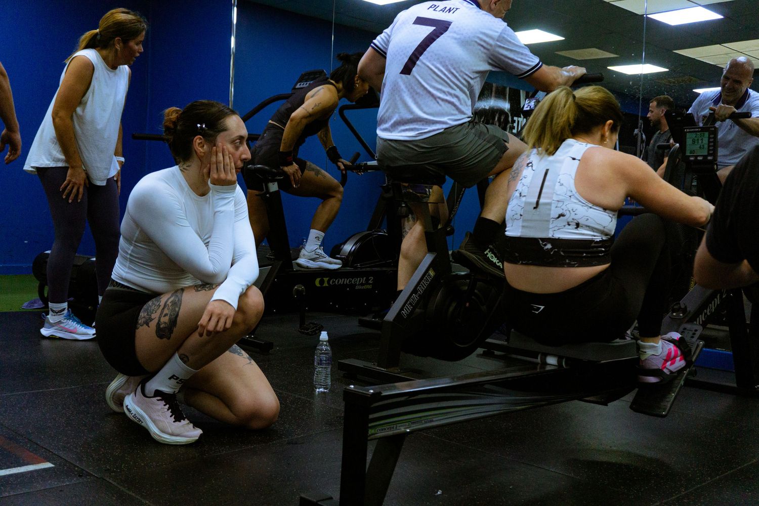 Group of people exercising on rowing machines and bikes in a busy gym fitness class.