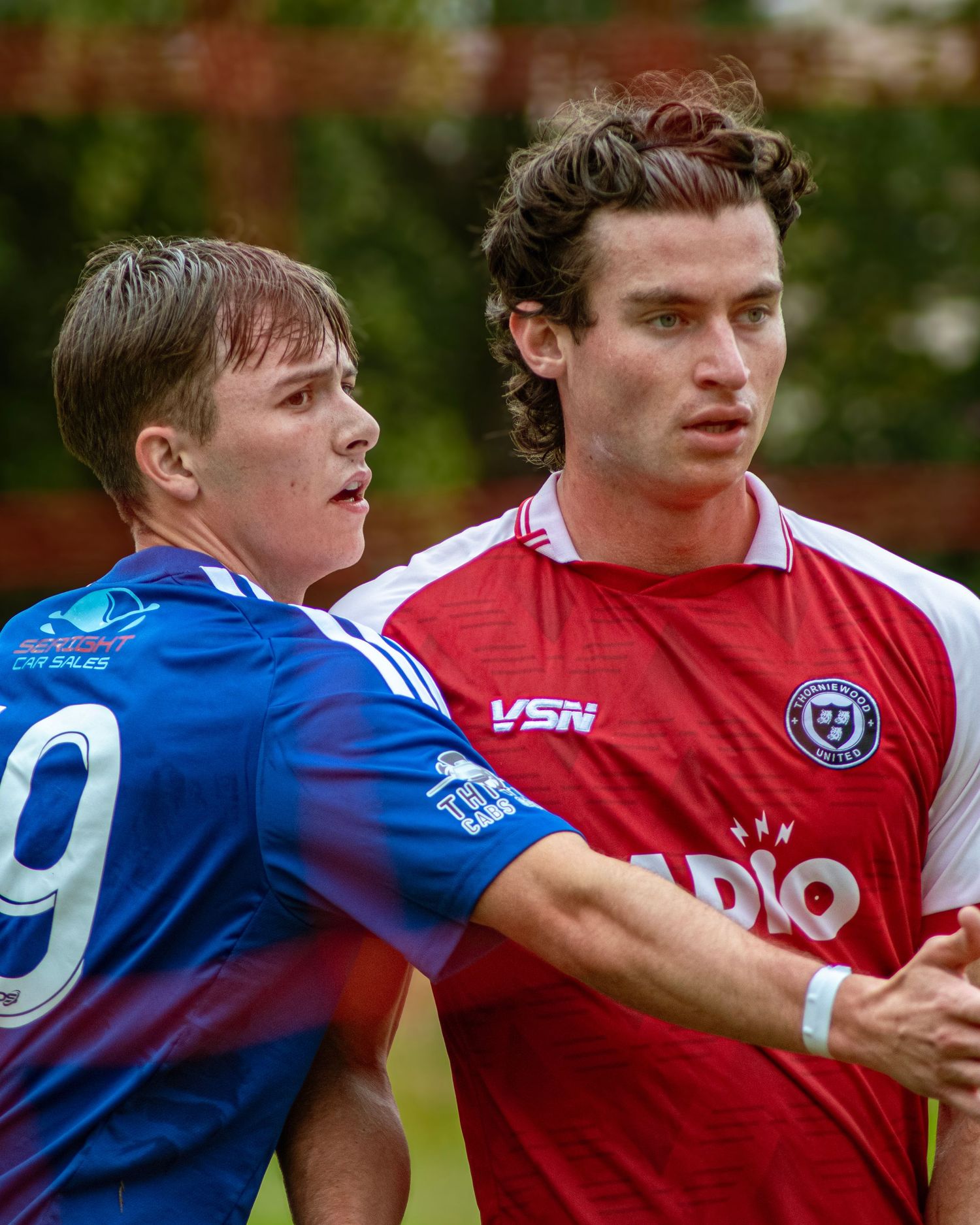 Two soccer players in blue and red jerseys compete during a match on a grass field.