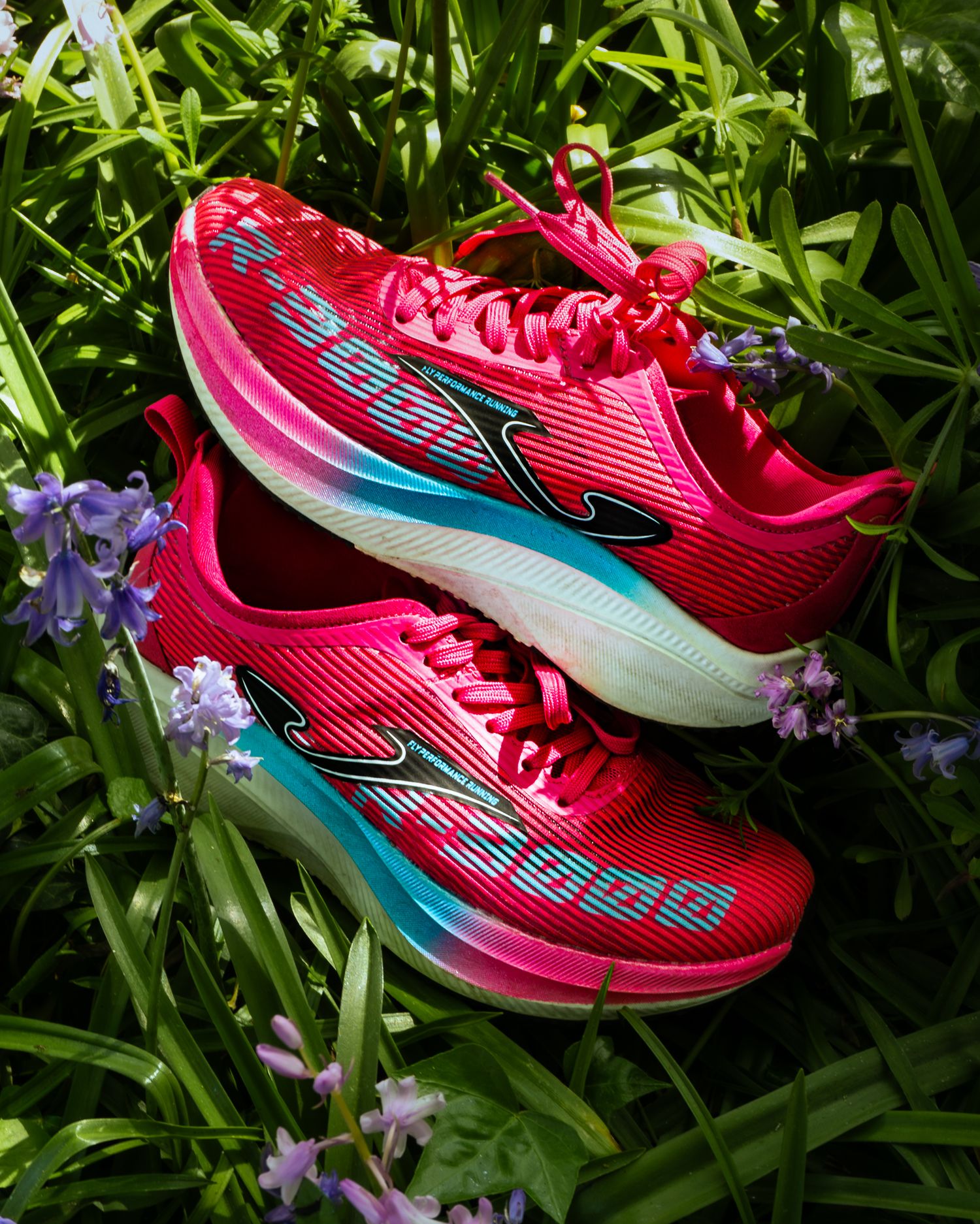Pair of bright pink Joma R-3000 running shoes resting among green foliage and purple flowers.