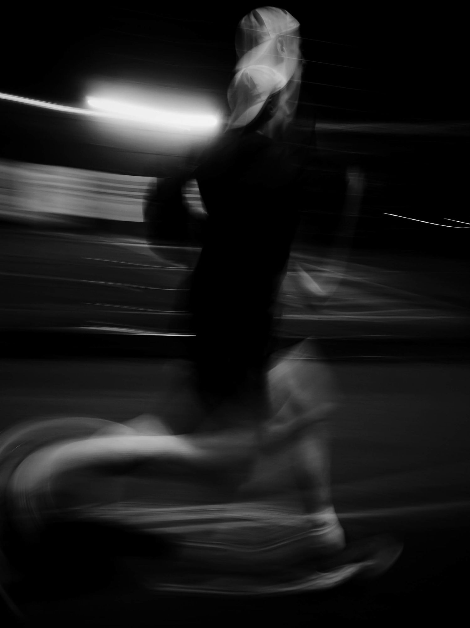 Black and white motion blur photo of a female runner sprinting at night on a track.