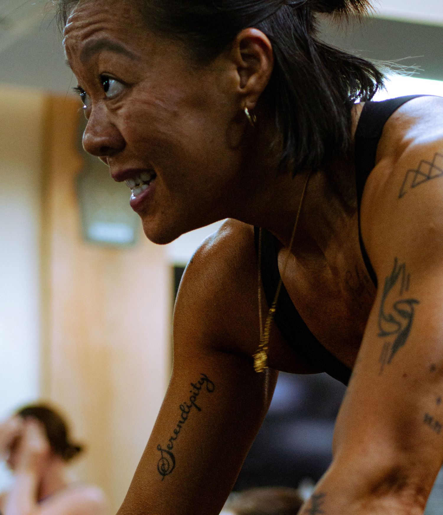 Tattooed woman leaning forward during intense workout session in gym.