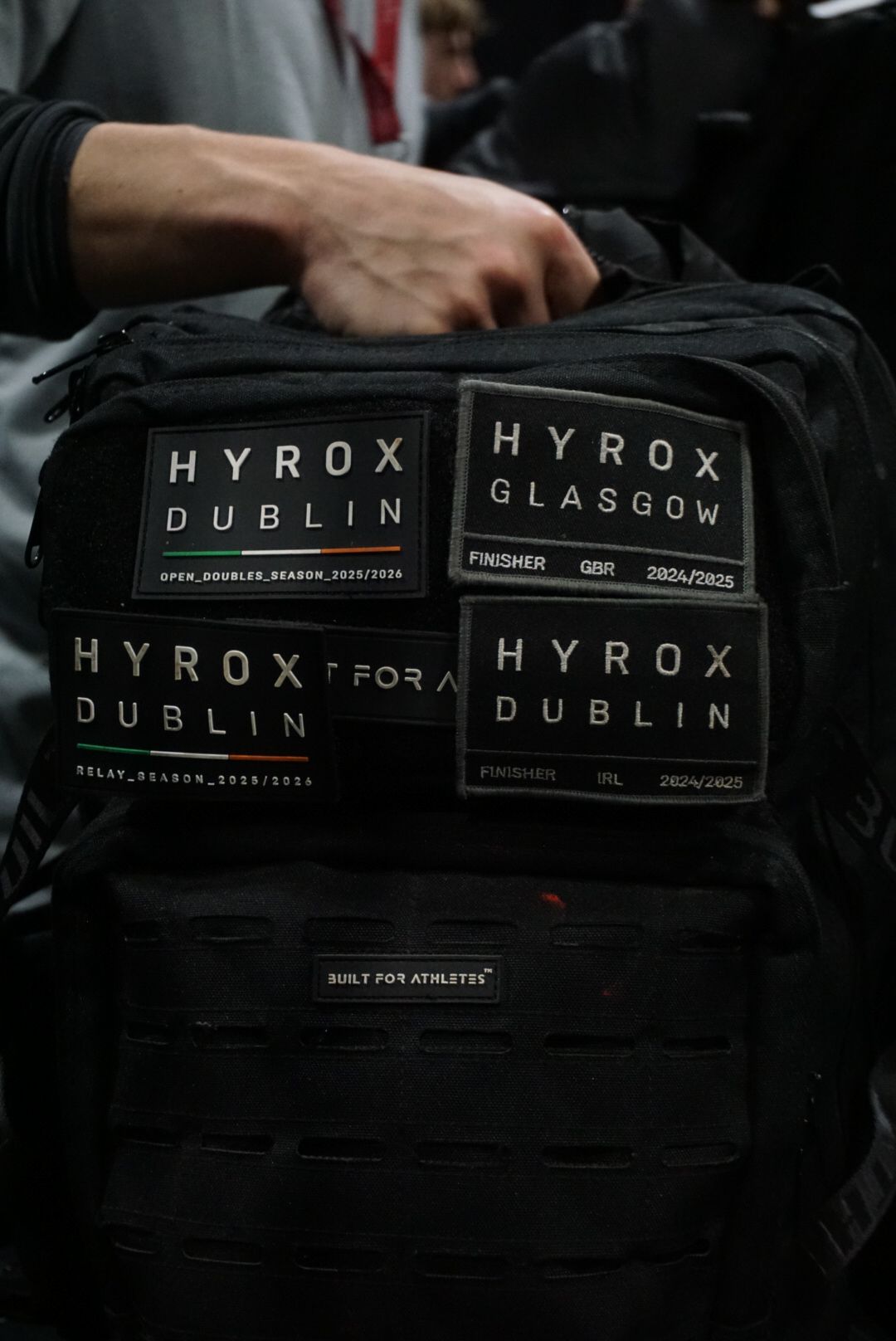 Black athletic backpack covered with HYROX Dublin and Glasgow finisher patches at competition.