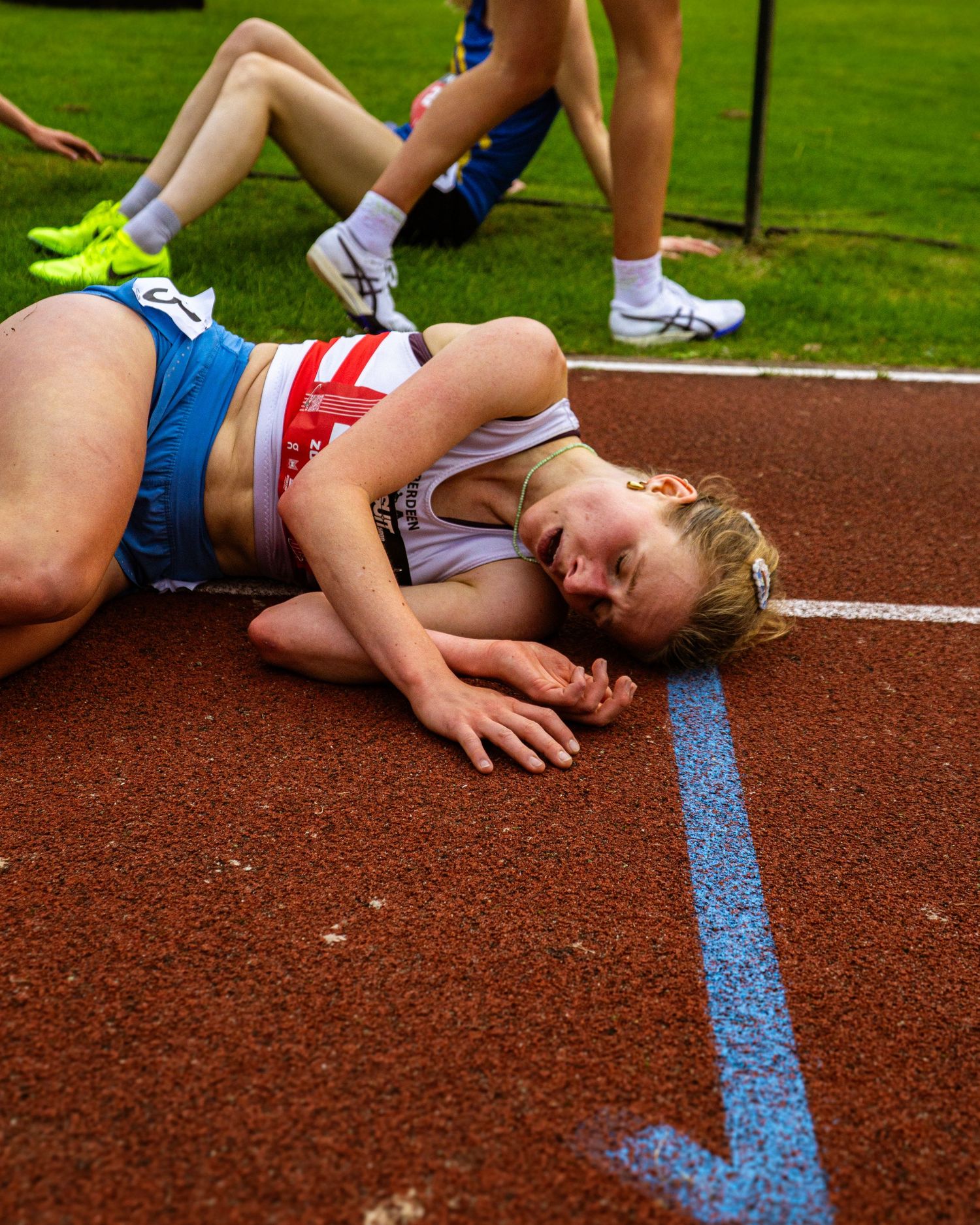 Exhausted female runner lies on red athletics track after race, showing emotion at outdoor competition.