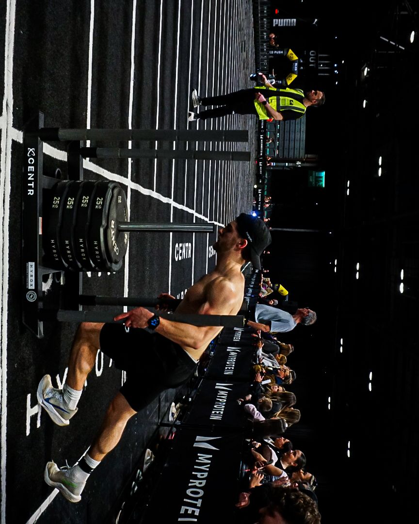 Athlete performs a muscle-up on gymnastics rings at a HYROX fitness competition event.
