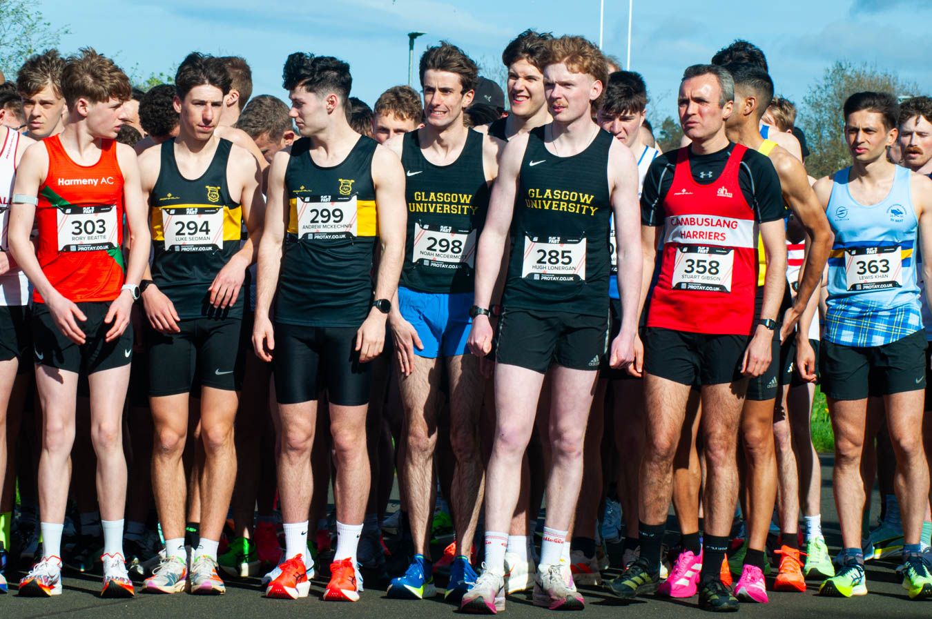 Large group of male runners in athletic gear lined up at the start of a road race.