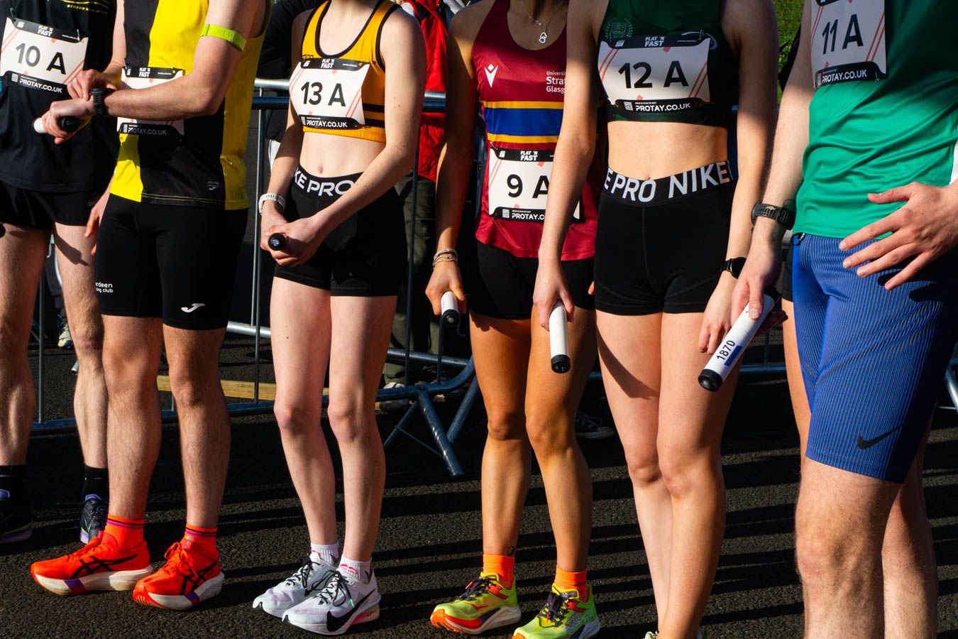 Athletes lined up at race start wearing numbered bibs and colorful running shoes on track.