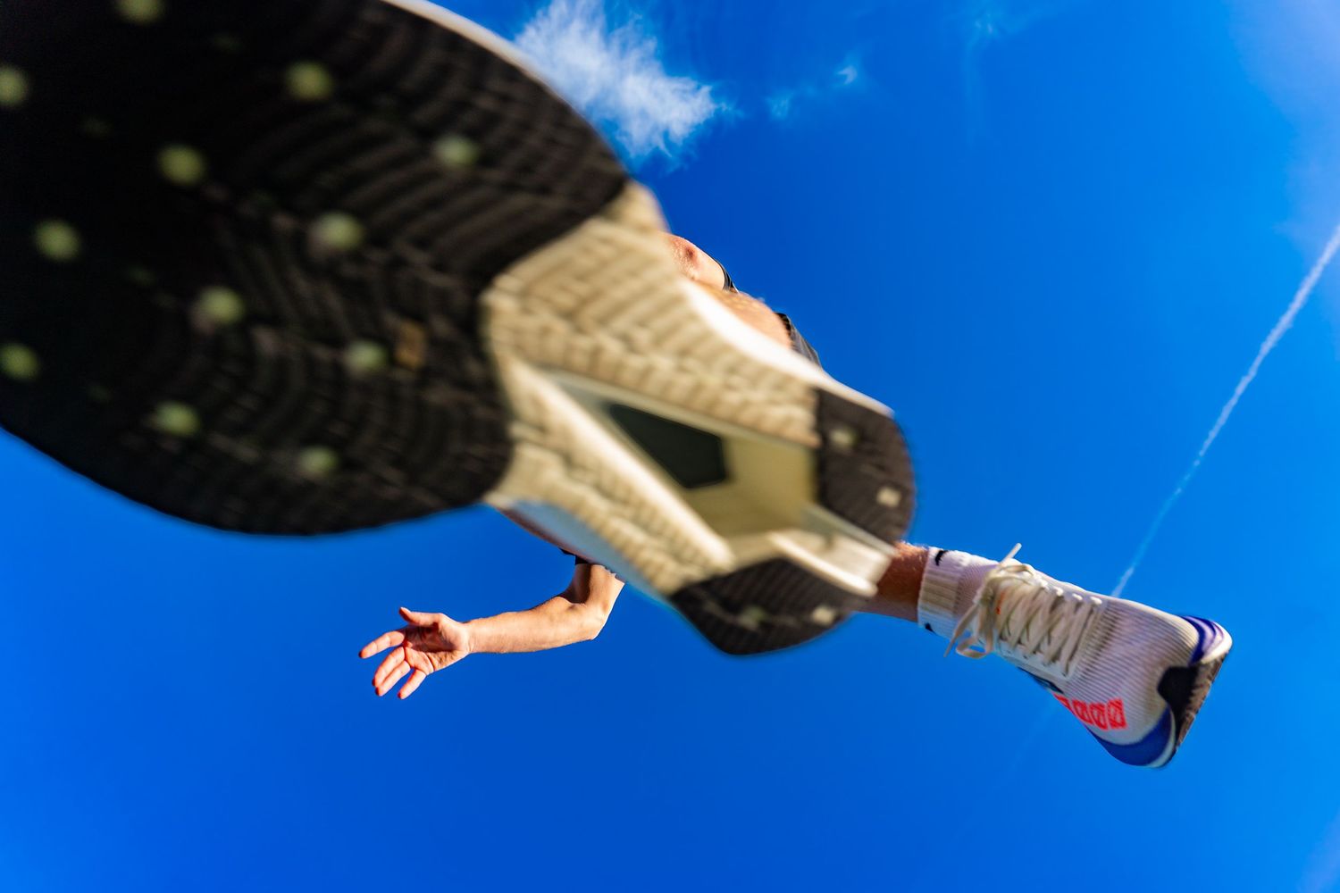 Dramatic worm's-eye view of a runner's shoe sole mid-stride against a clear blue sky.