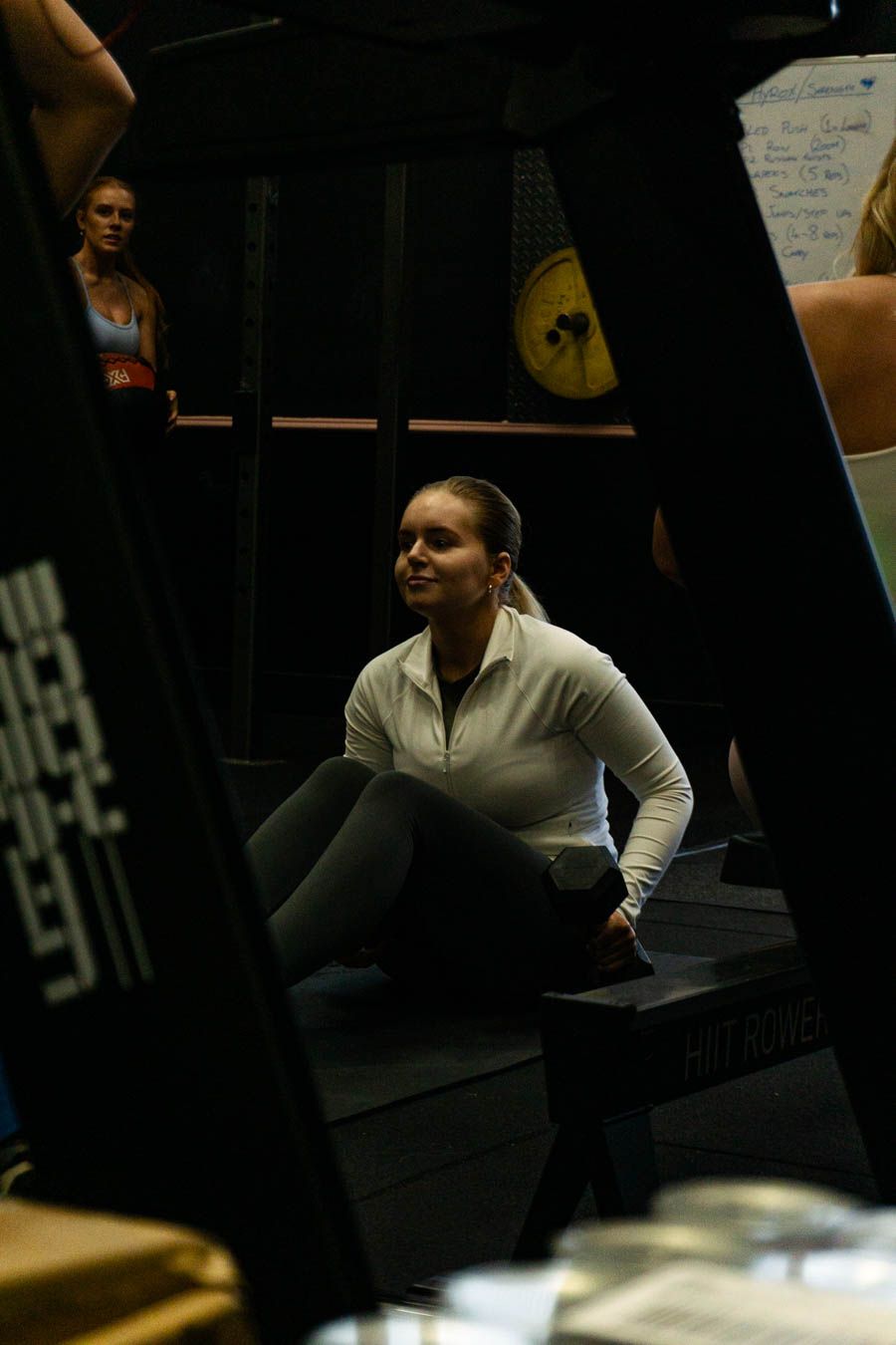 Woman in white jacket sitting on gym steps in a dark gym.