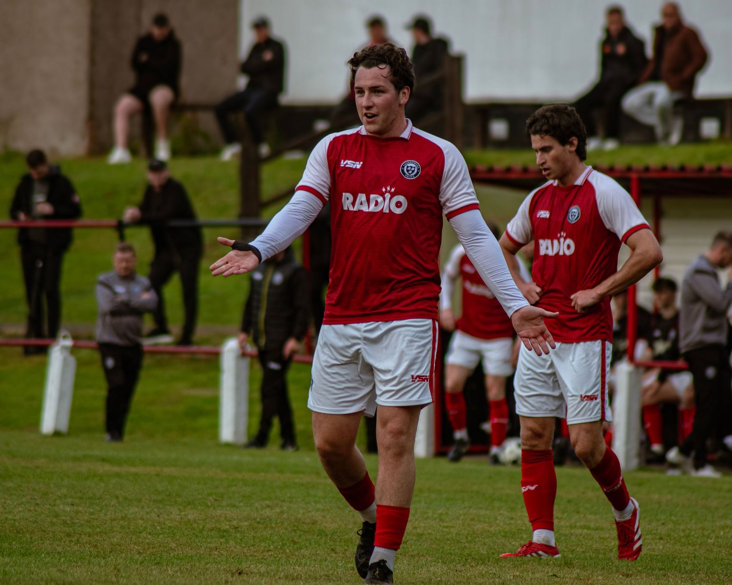 A footballer in a red and white Radio jersey gestures on the pitch during a match.