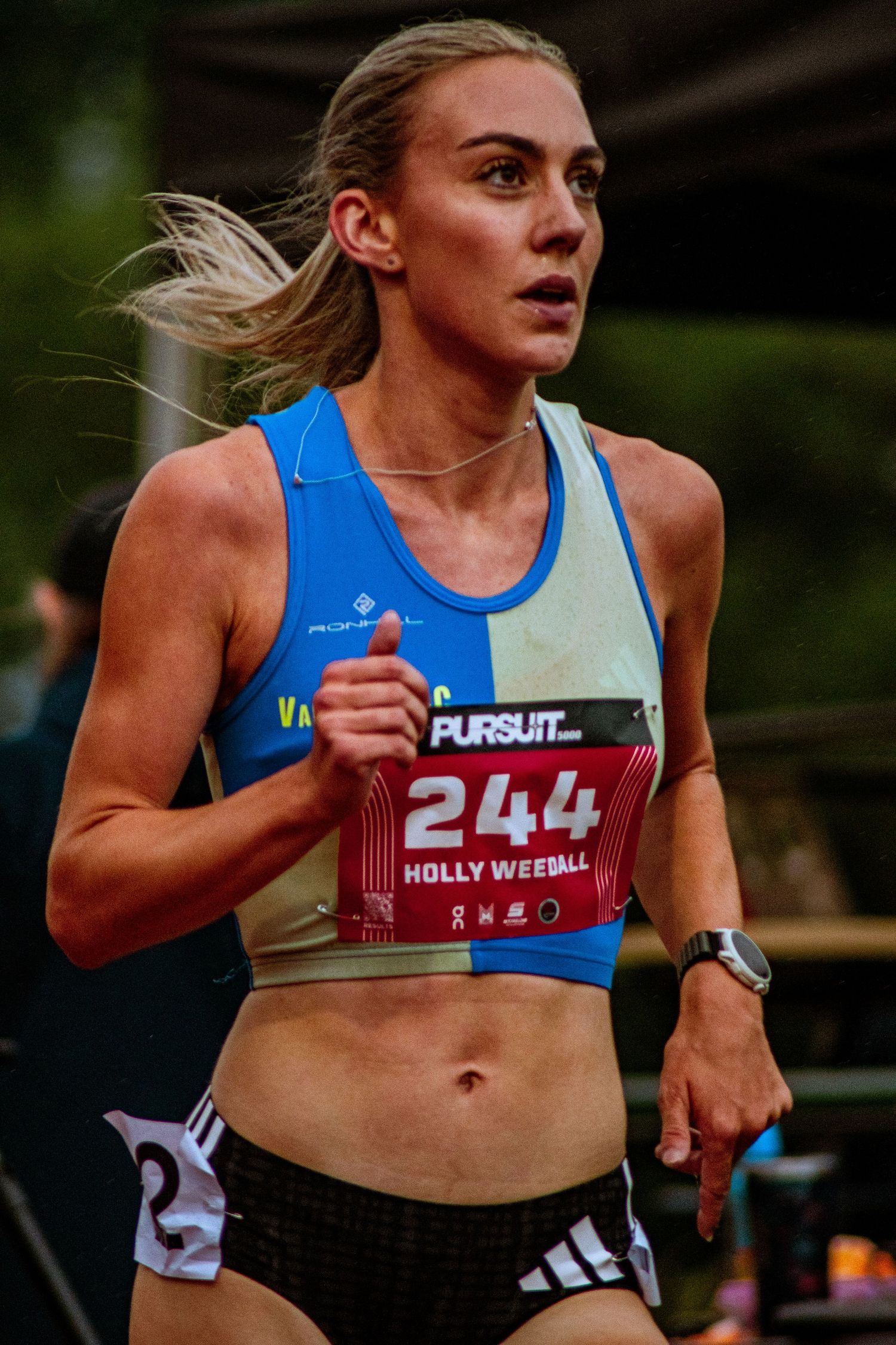 Runner Holly Weedall wearing bib number 244 competes in a road race wearing a blue and yellow athletic vest.
