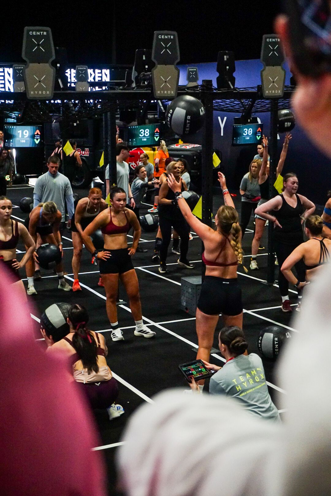 Female athletes performing wall ball exercises in a large CrossFit competition with crowd watching.
