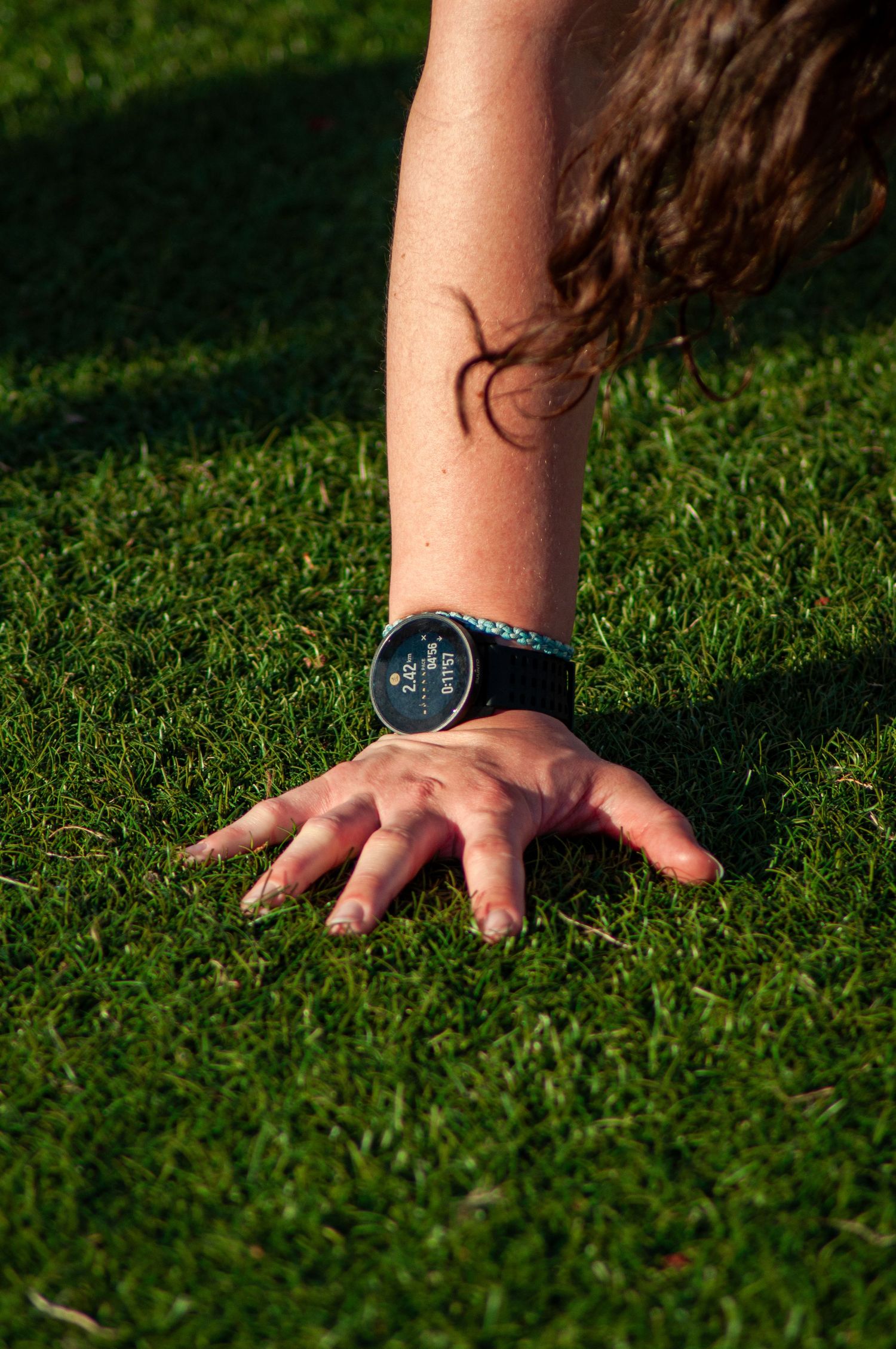 Close-up of a hand on green grass wearing a sports smartwatch with a tattoo visible on the forearm.