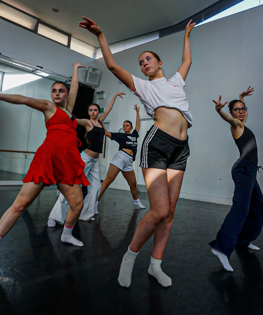 Group of dancers practice contemporary dance moves in a bright mirrored studio during rehearsal.