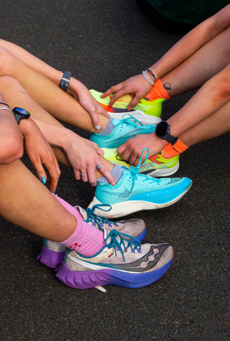 Runners sitting on pavement tying colorful athletic shoes before a race, wearing bright socks.