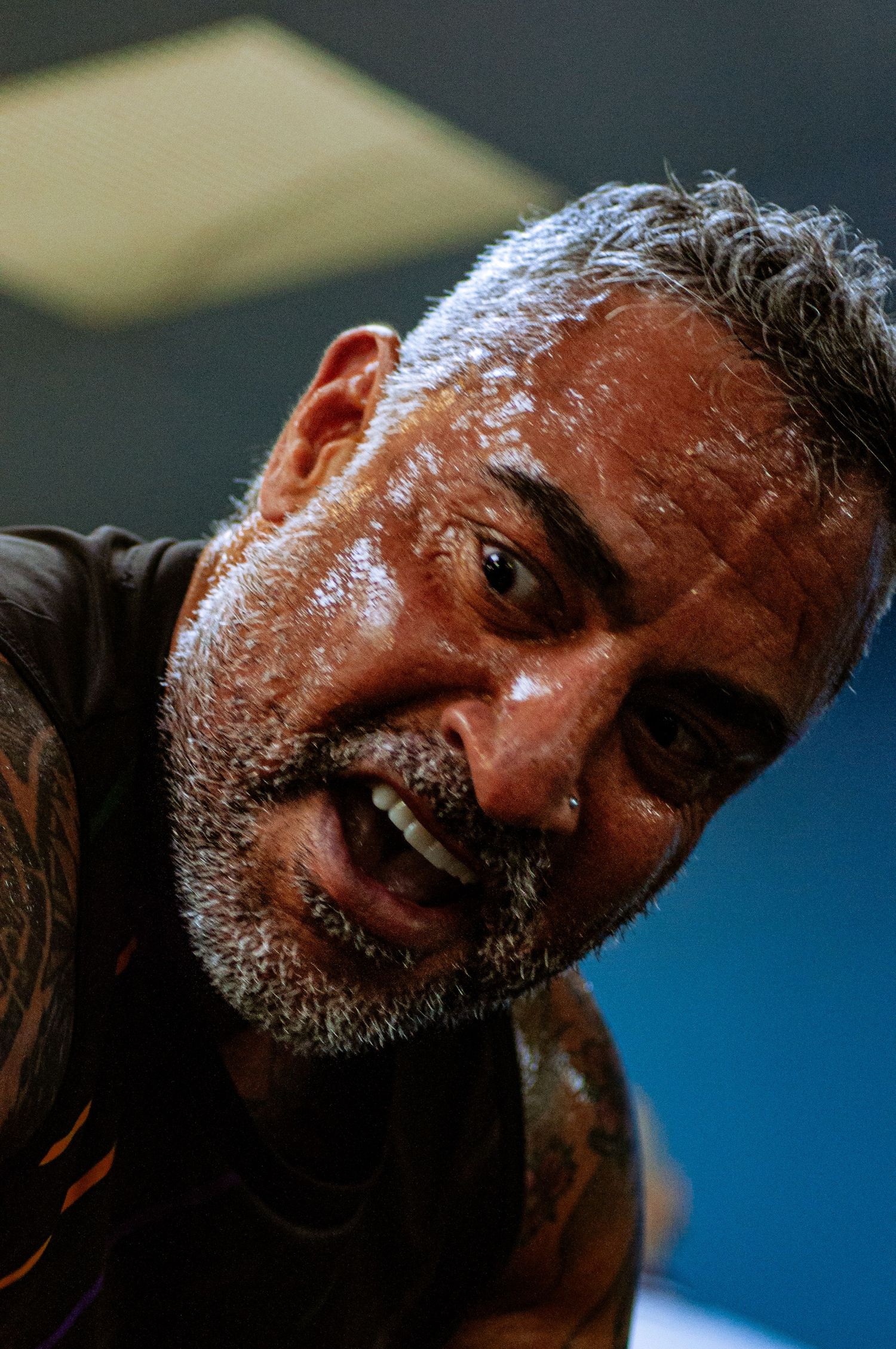 Sweaty tattooed man with gray beard smiling intensely during an intense workout session.