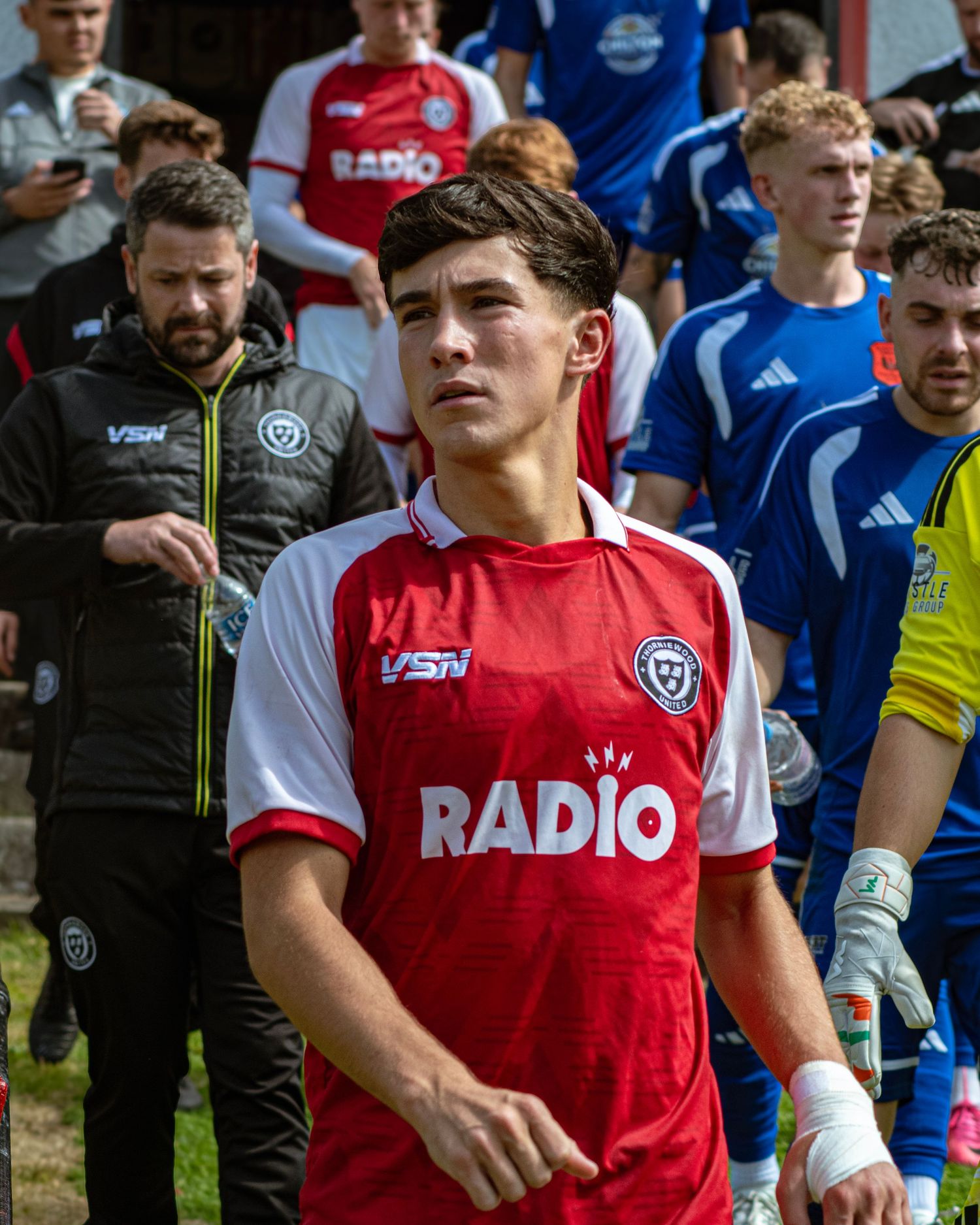 Young male footballer in a red Radio jersey walking out onto the pitch before a match.