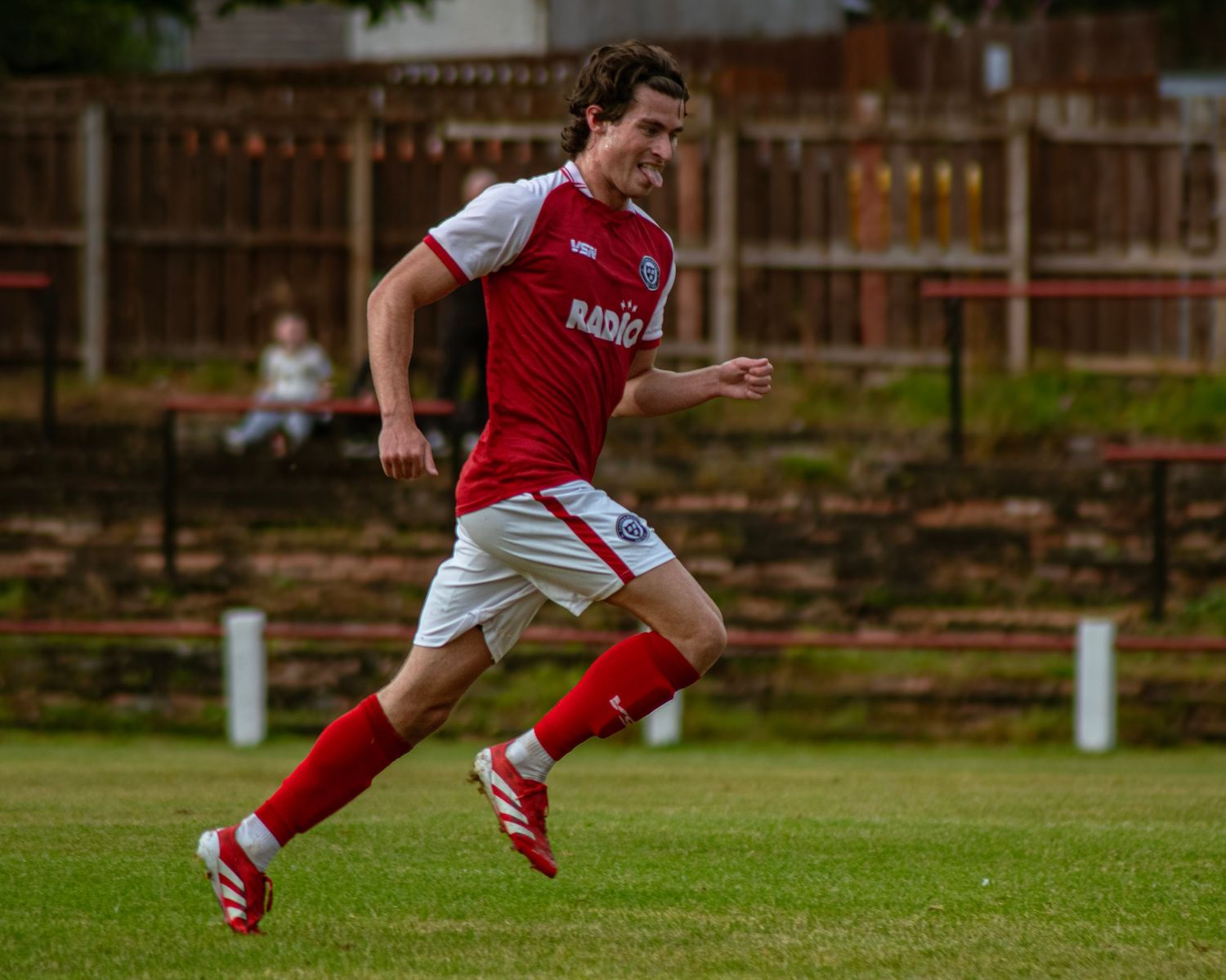 Soccer player in red and white kit sprinting on green grass field during a match.