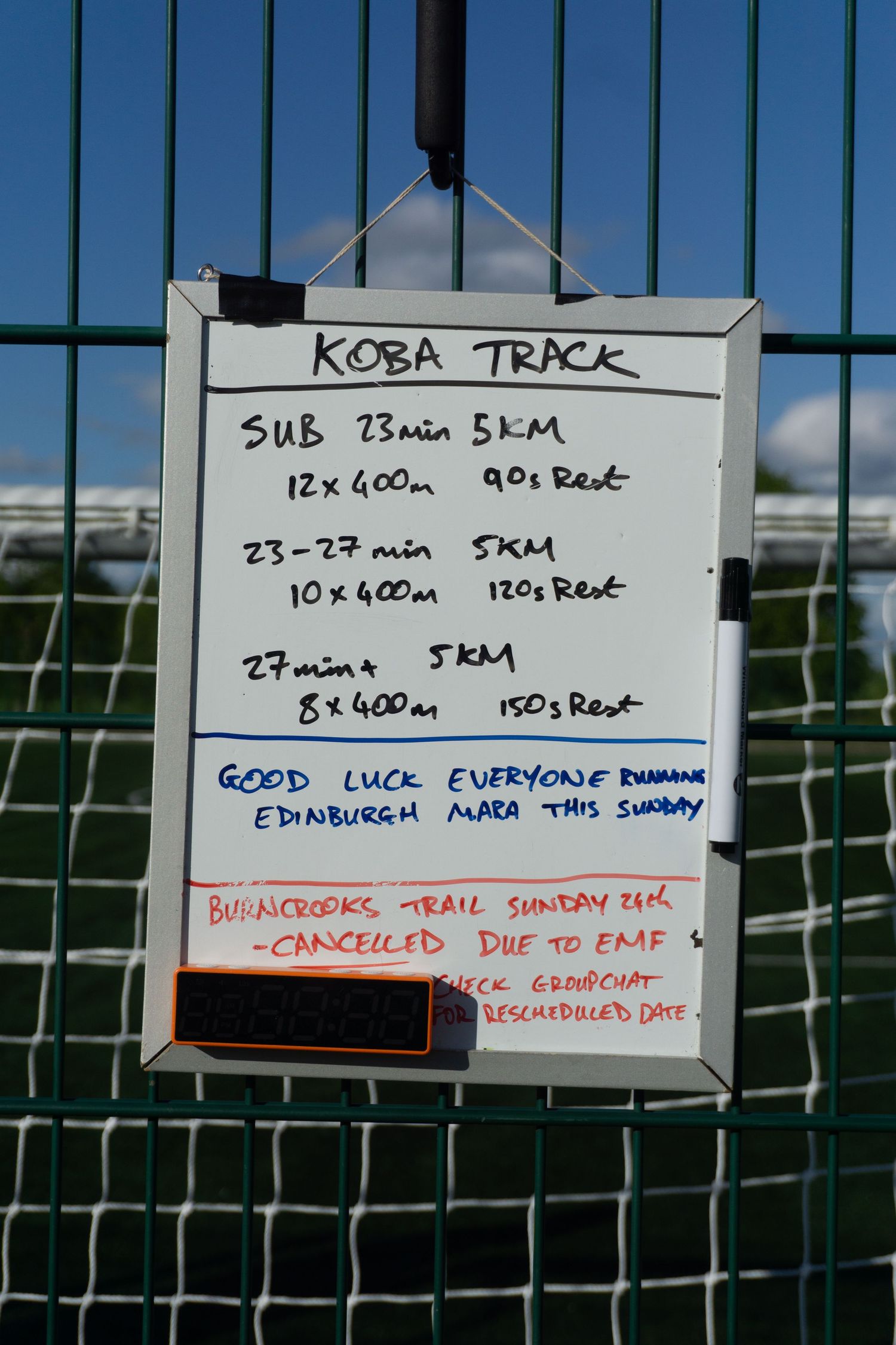 KOBA Track workout whiteboard showing 5KM training plans with 400m intervals and rest times.
